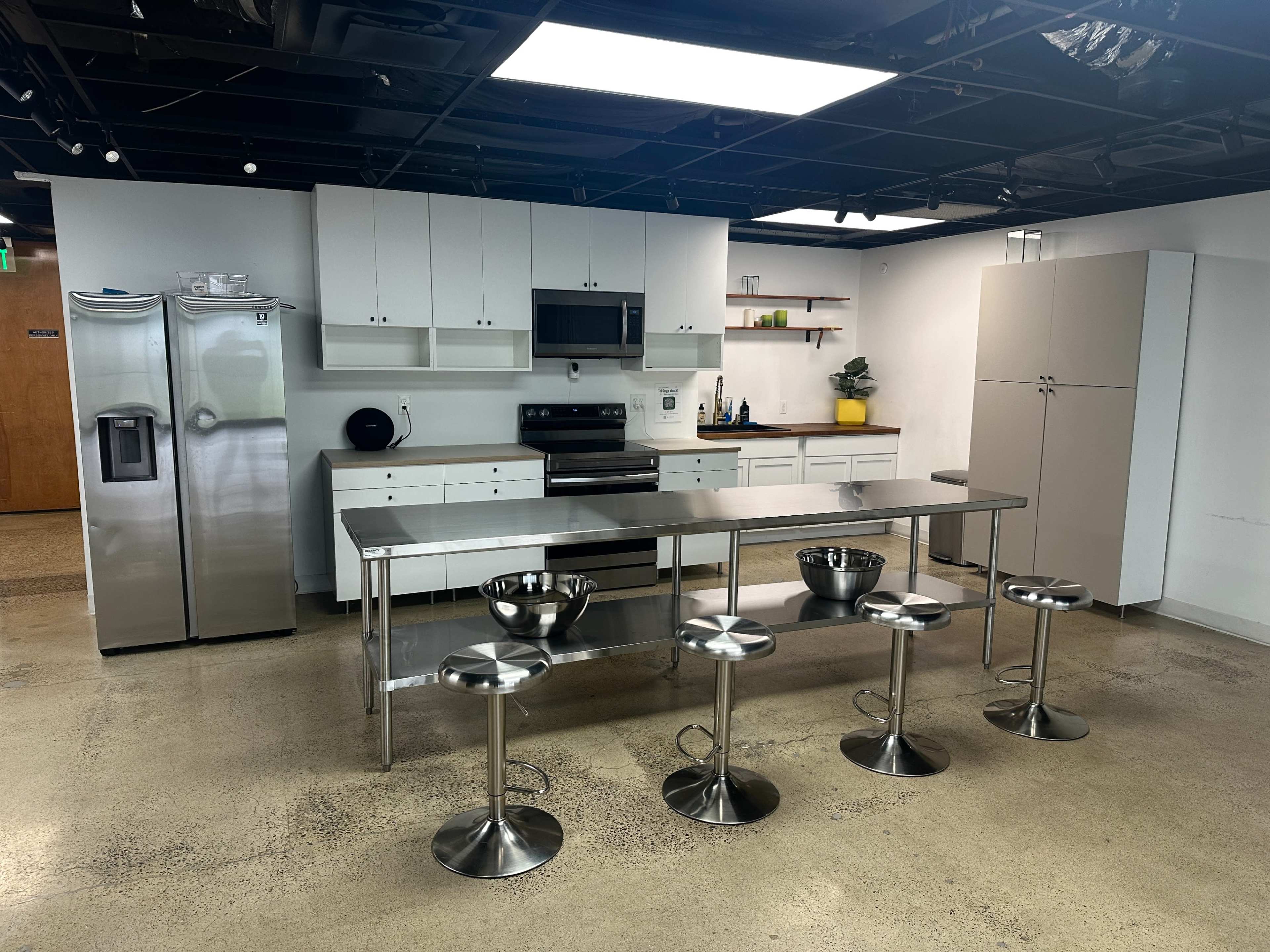 The image shows a modern kitchen setup with stainless steel appliances, a central island with stools, and minimalistic white cabinetry.