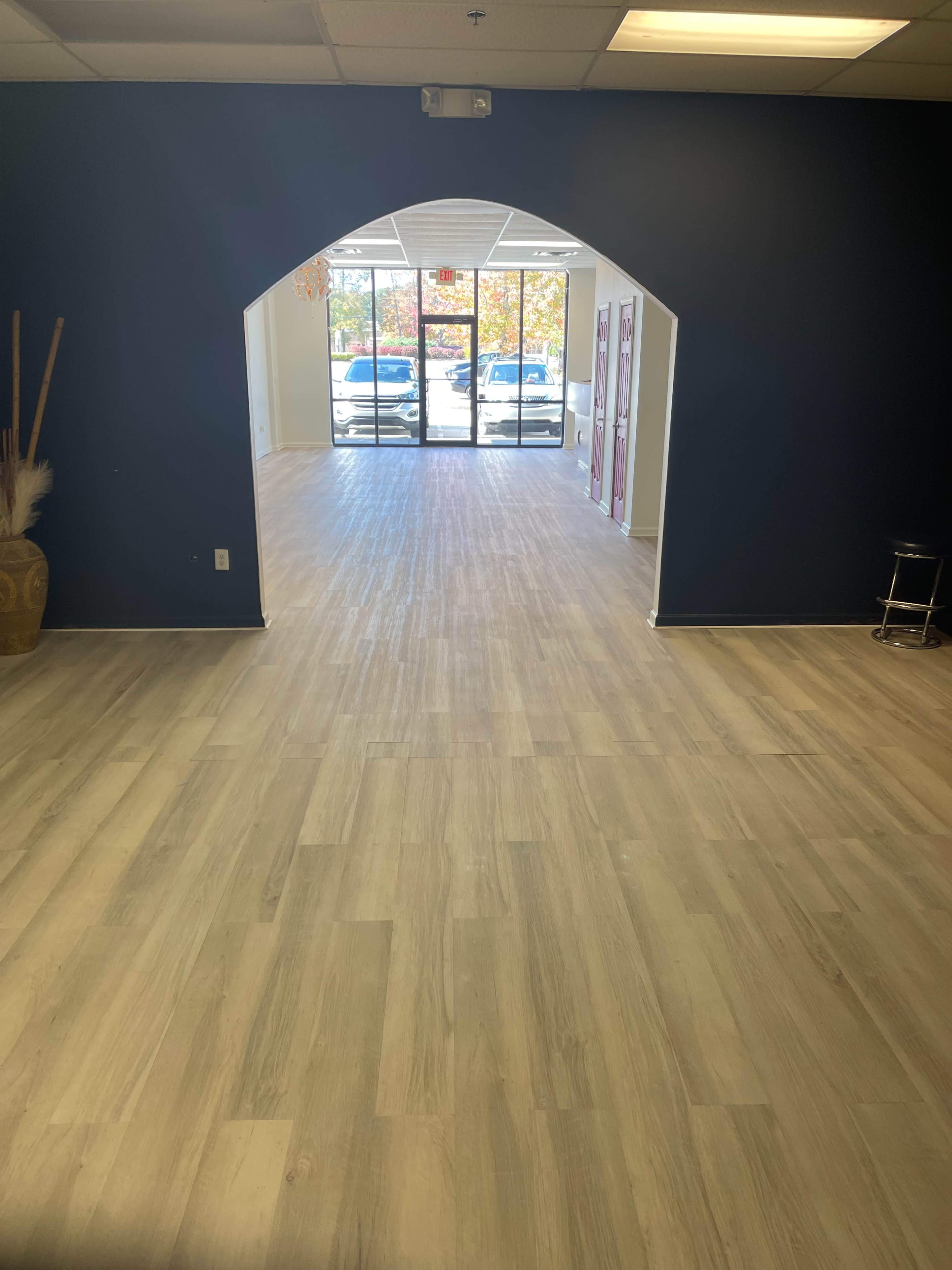 A spacious interior with large windows at the far end, featuring light-colored flooring and a dark blue wall archway.