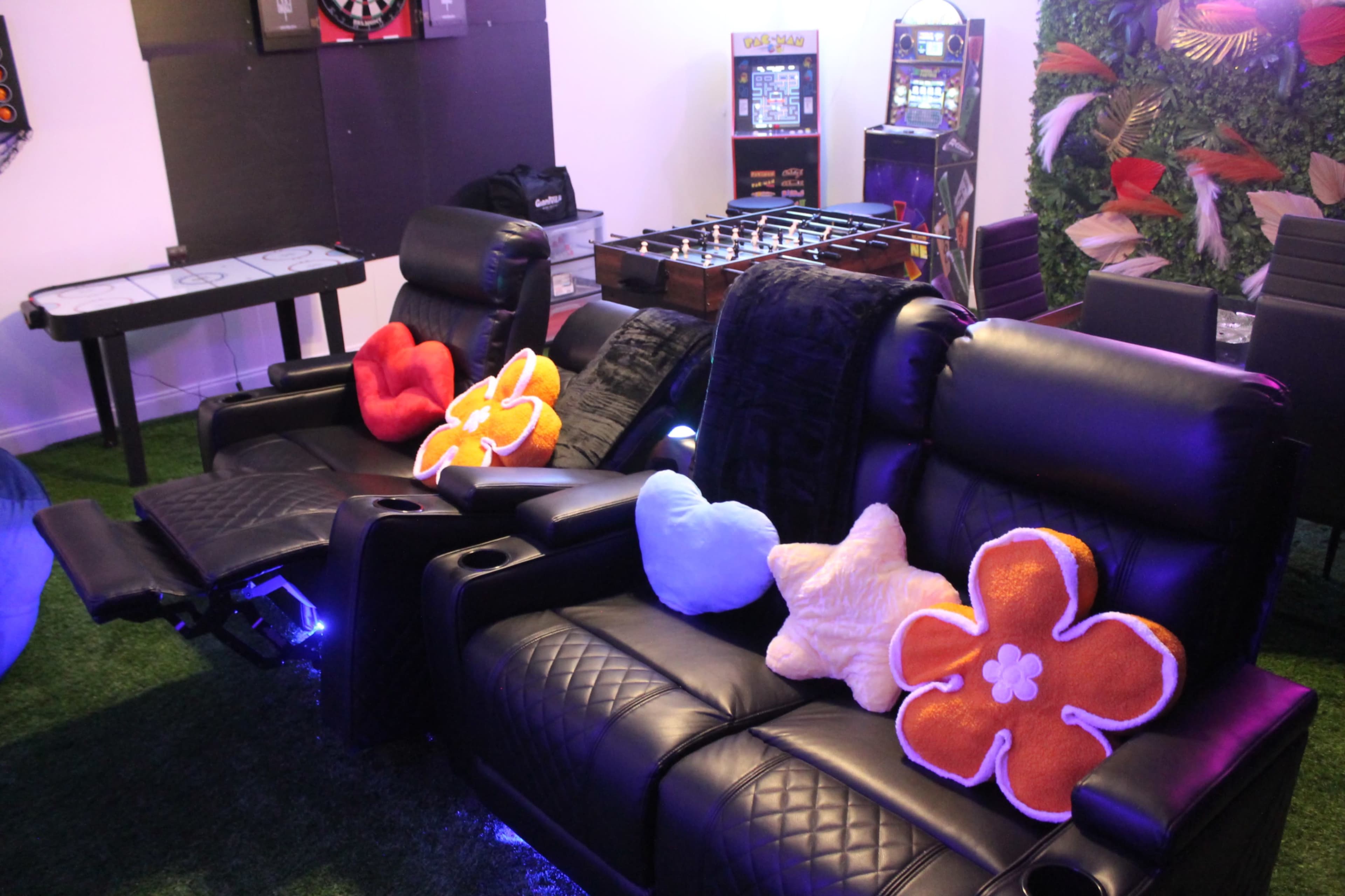 Black reclining chairs with colorful flower-shaped cushions in a game room featuring a dartboard and foosball table.