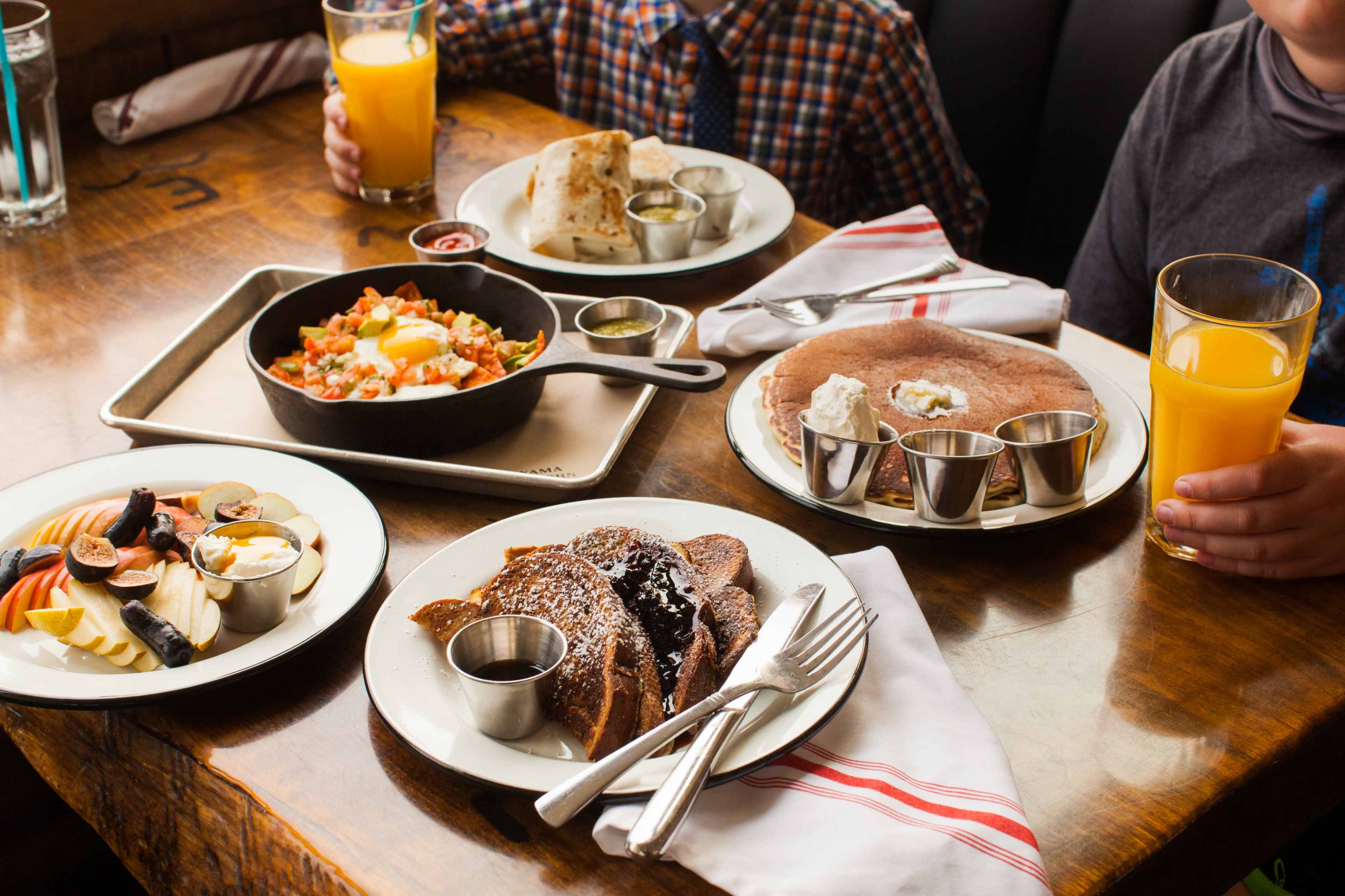 The table displays a variety of breakfast dishes, including French toast, a vegetable hash with an egg, and fruit sides, along with two glasses of orange juice.