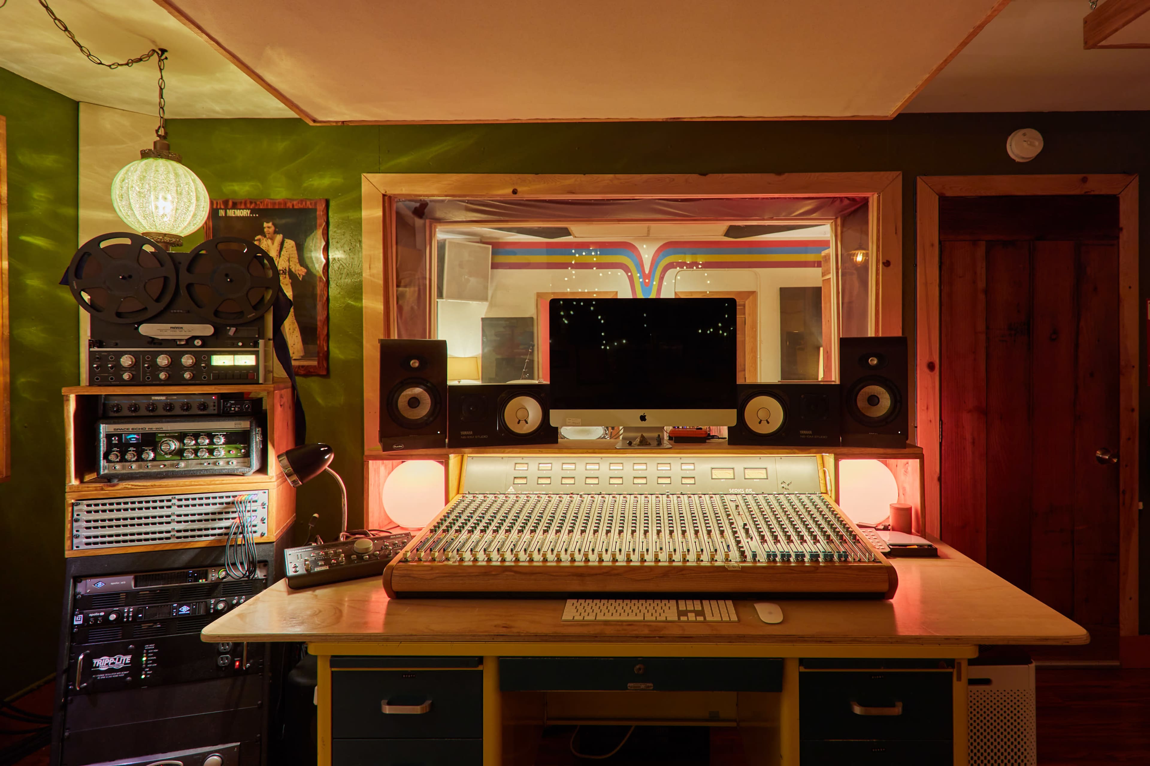 The image shows a recording studio with a large mixing console, audio equipment racks, and monitors, illuminated by soft lighting.