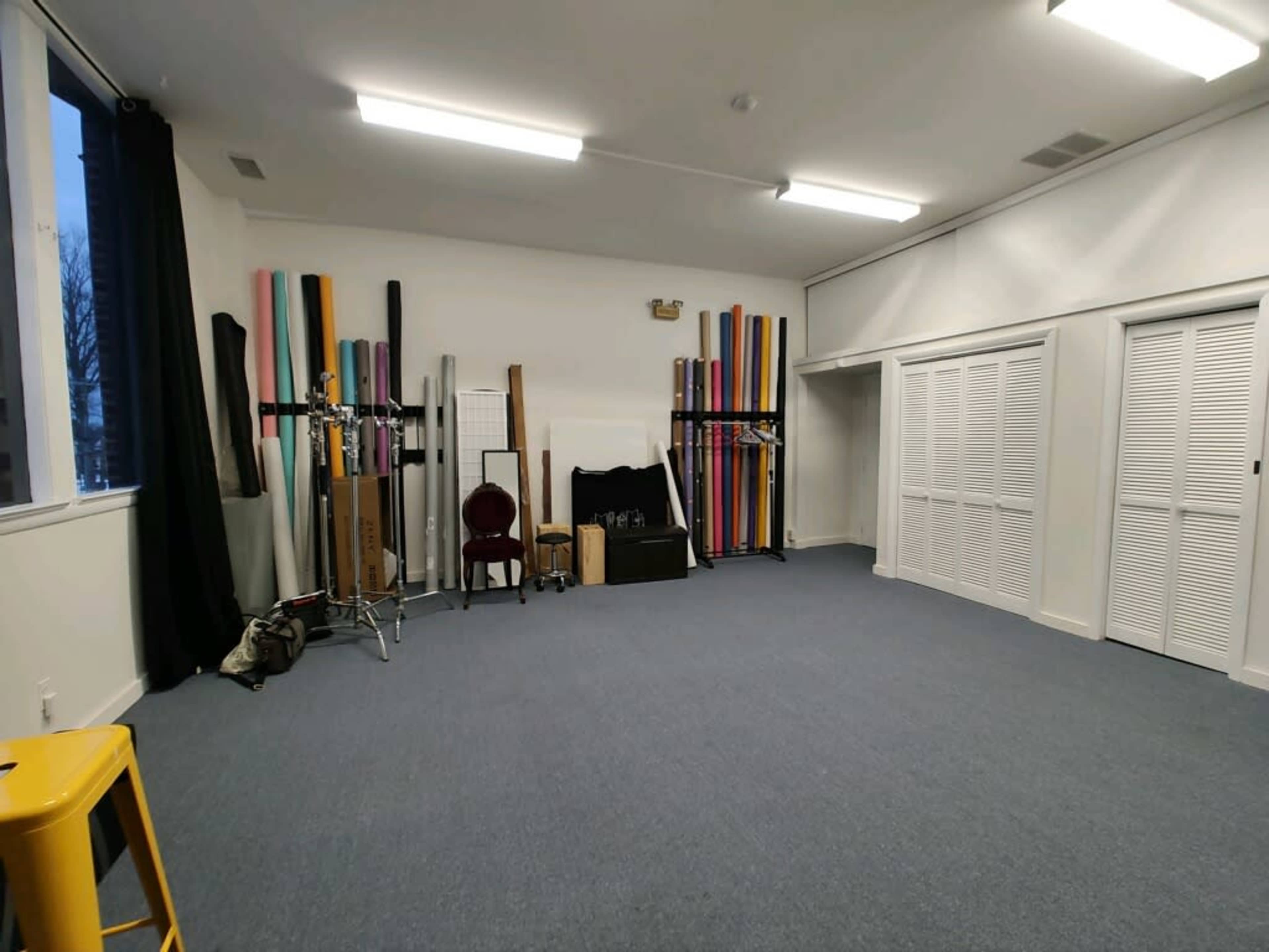 A spacious room with a blue carpet, featuring a rack of rolls in various colors, a chair, and equipment neatly arranged against one wall.