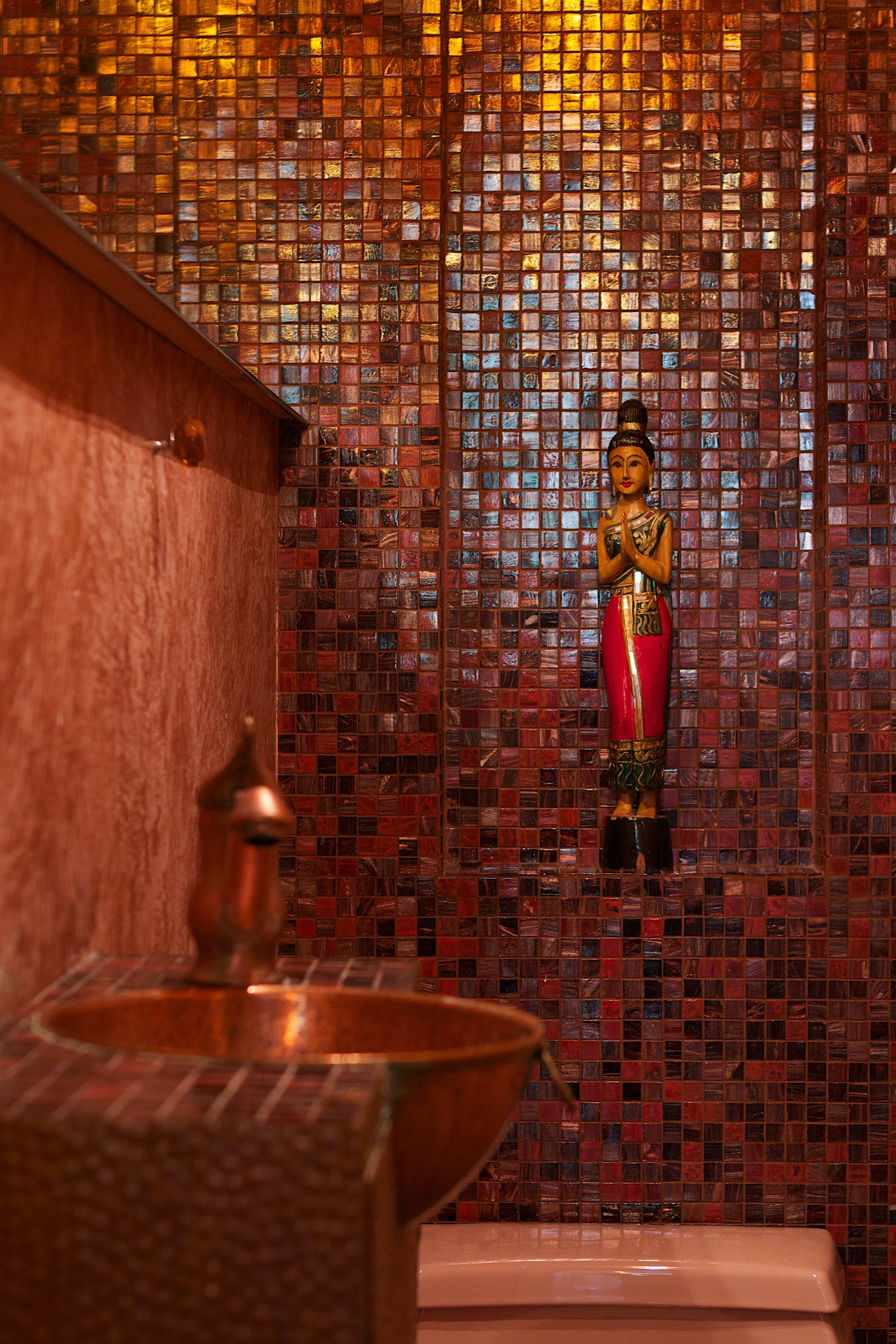 A decorative bathroom features a mosaic tile wall, a small statue of a woman, and a metallic sink.