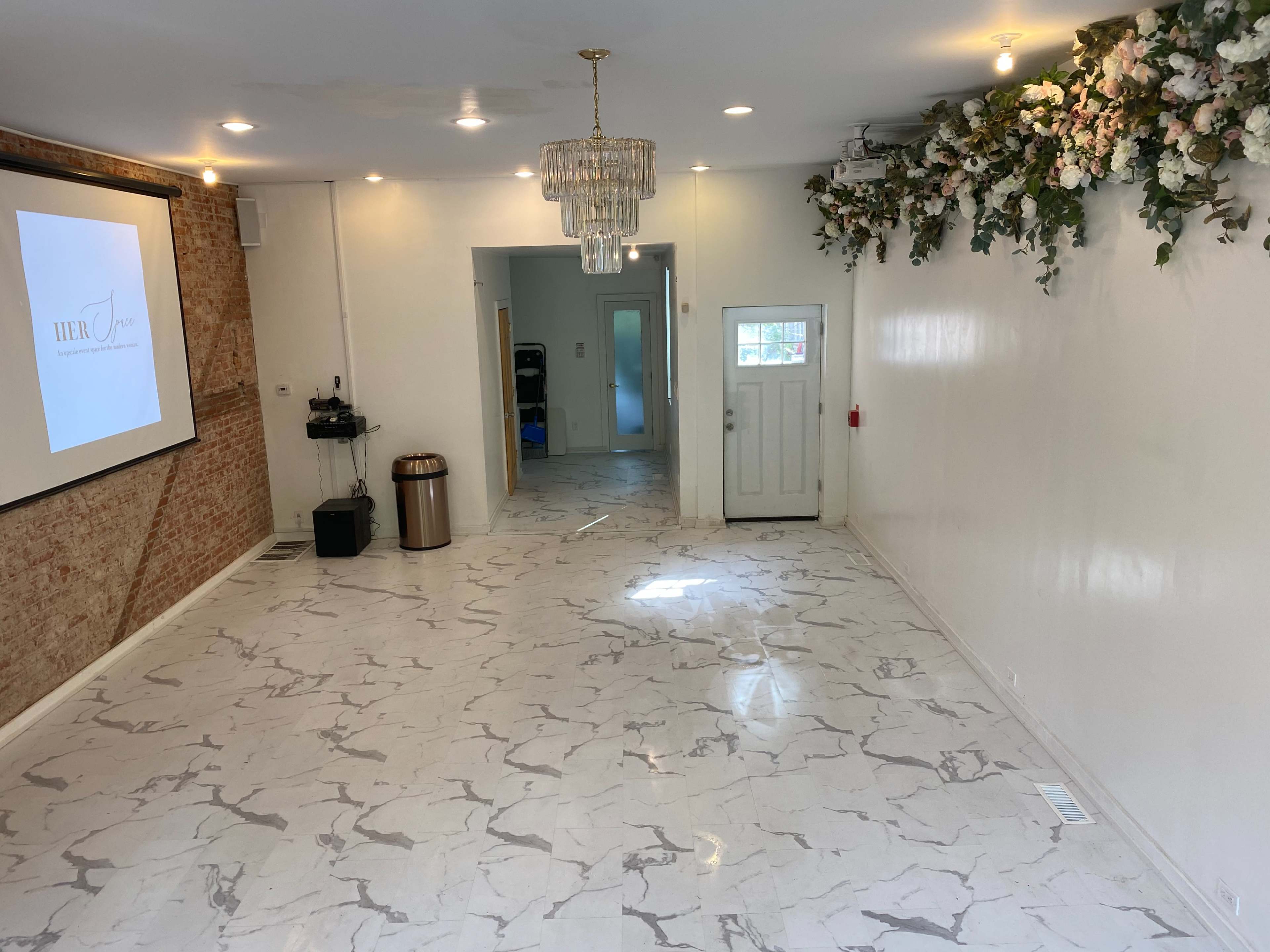 The interior of a spacious room features a marble-patterned floor, a crystal chandelier, and floral decorations on one wall.