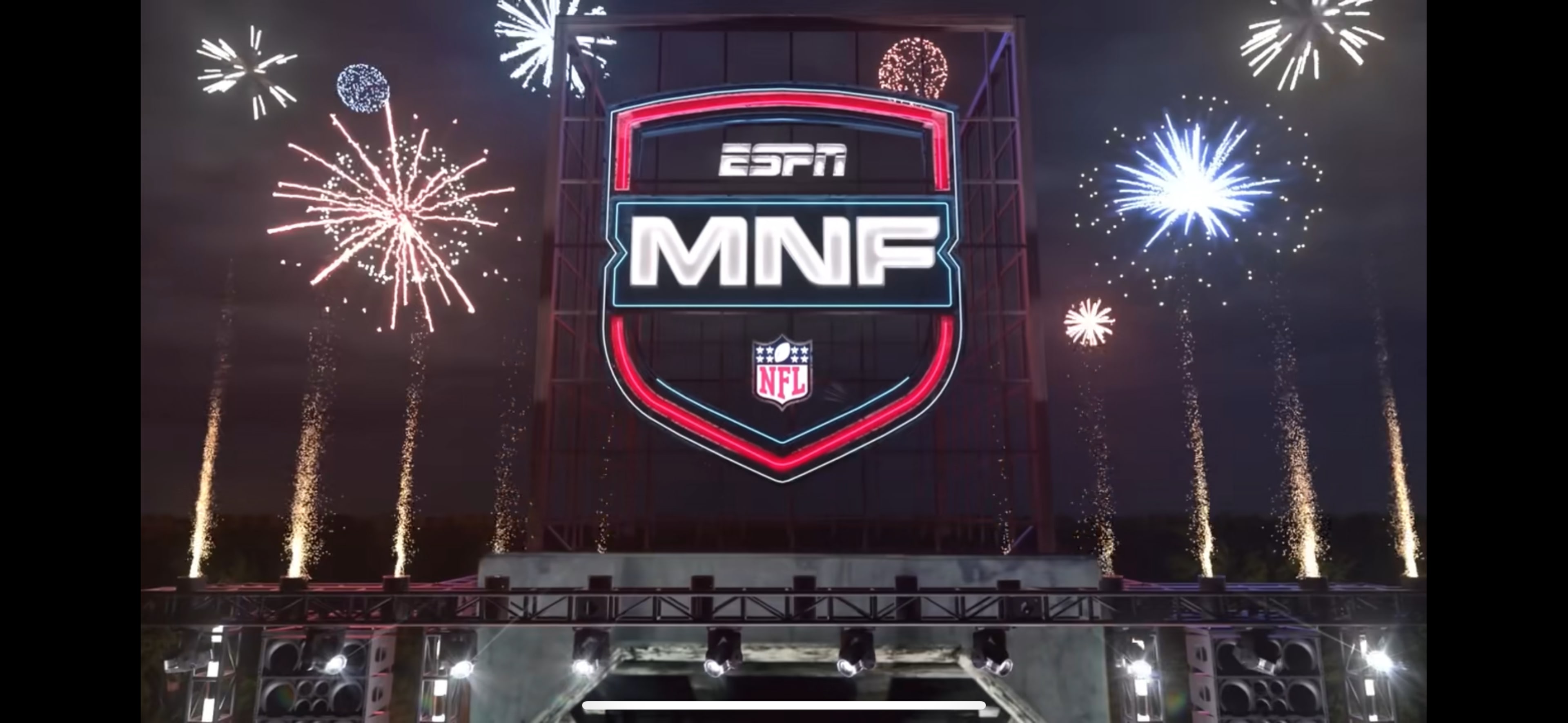 The image features a large illuminated sign displaying the ESPN Monday Night Football (MNF) logo, surrounded by fireworks in a nighttime setting.