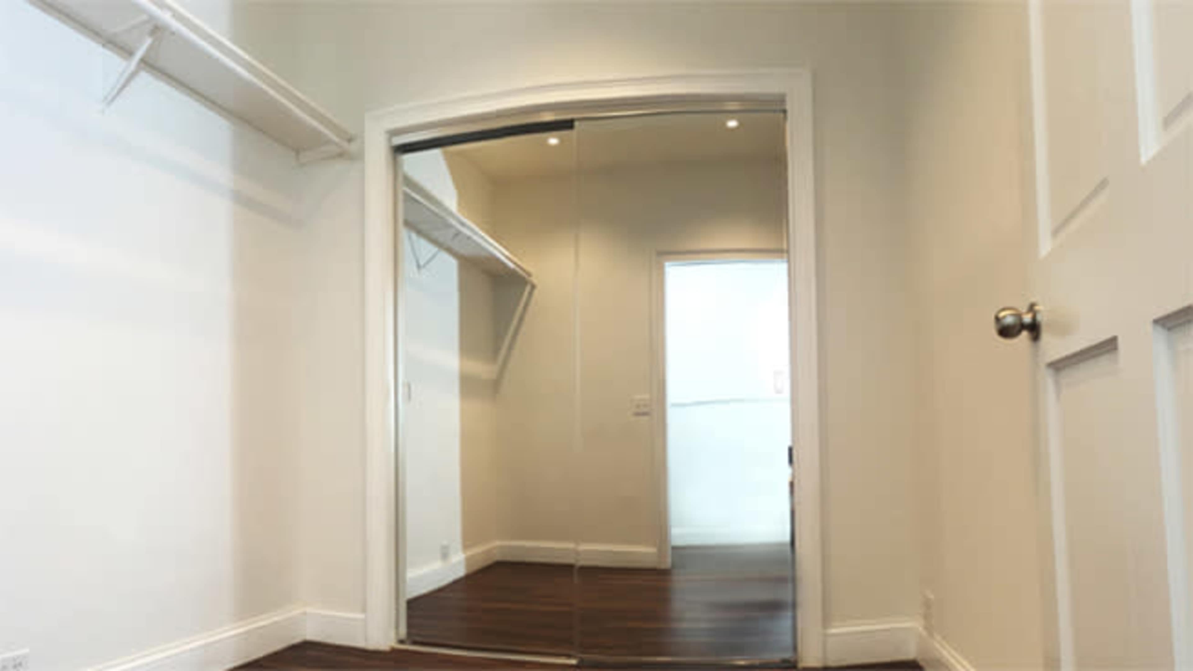 A small room with mirrored closet doors, a plain white wall, and a door leading to another space.