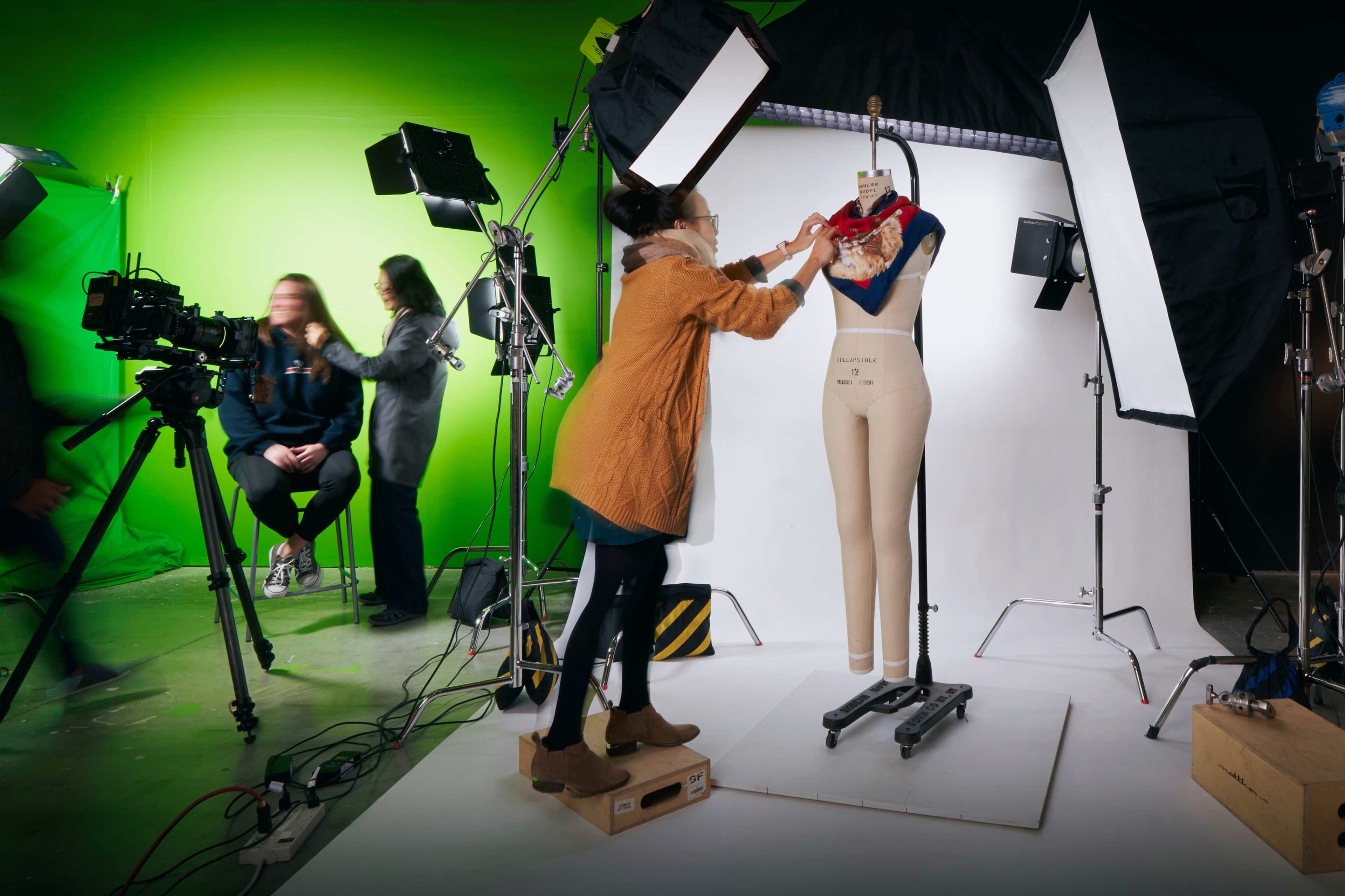 A person adjusts a scarf on a mannequin in a photography studio with green and white backgrounds and multiple lighting setups.
