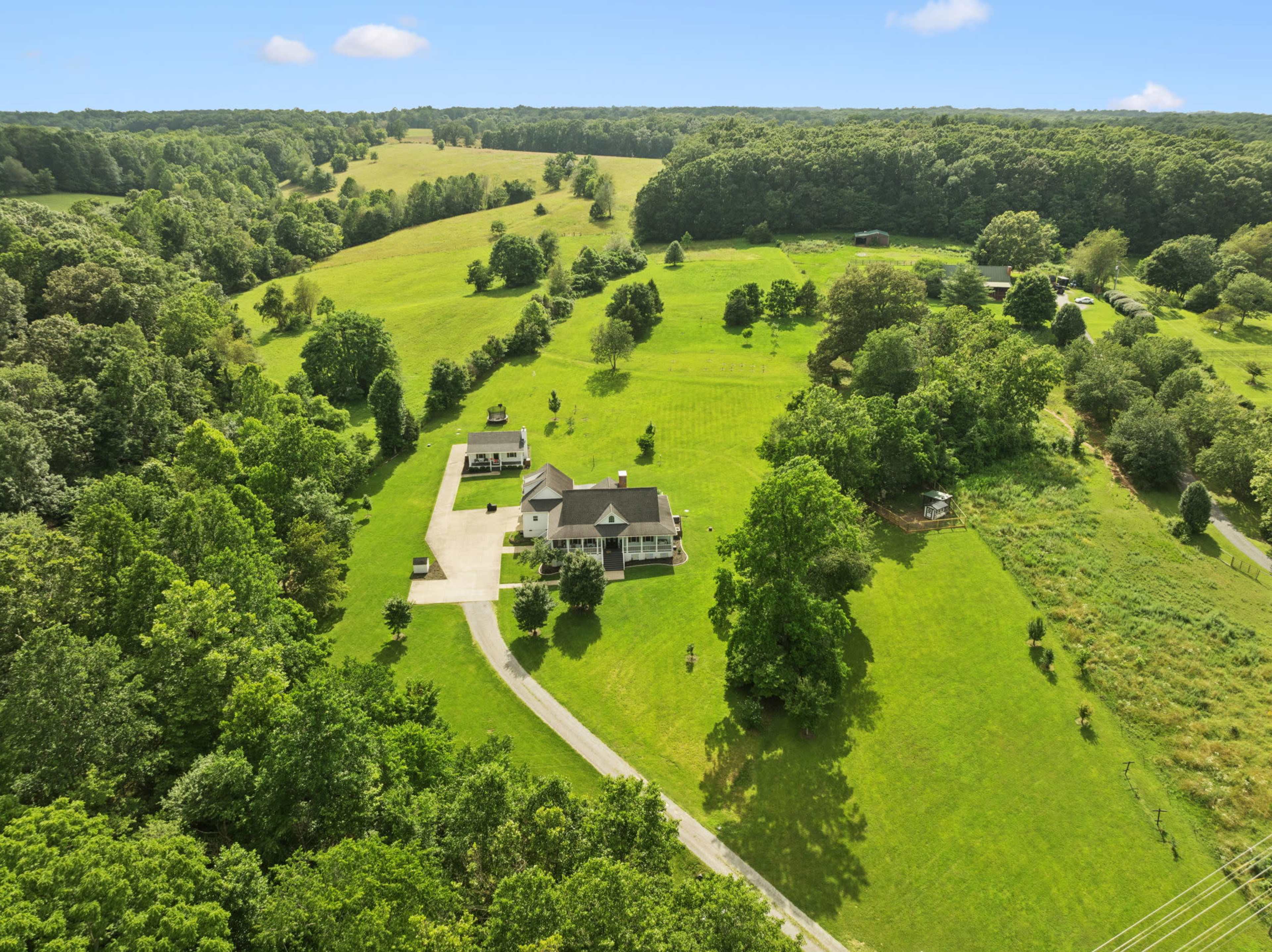 The image shows a large, green landscape with rolling hills and a house situated along a curved driveway, surrounded by trees.