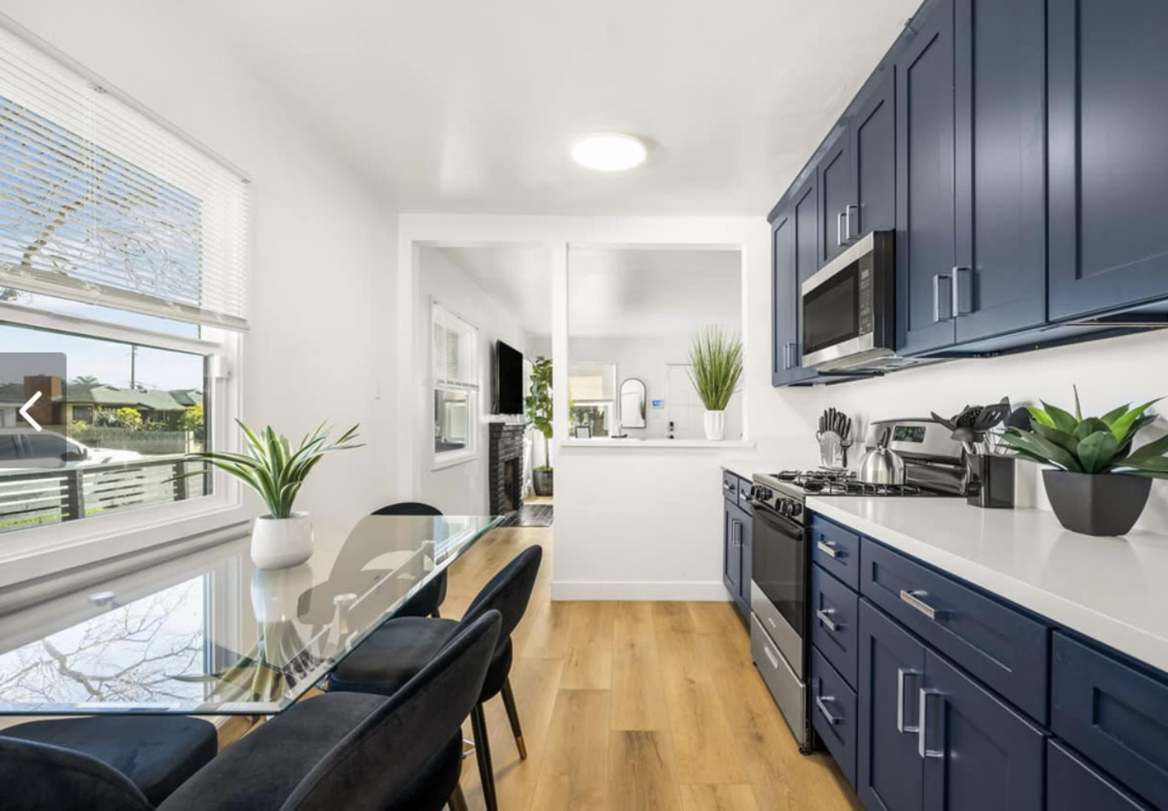 A modern kitchen features navy blue cabinets, stainless steel appliances, and a glass dining table with black chairs.