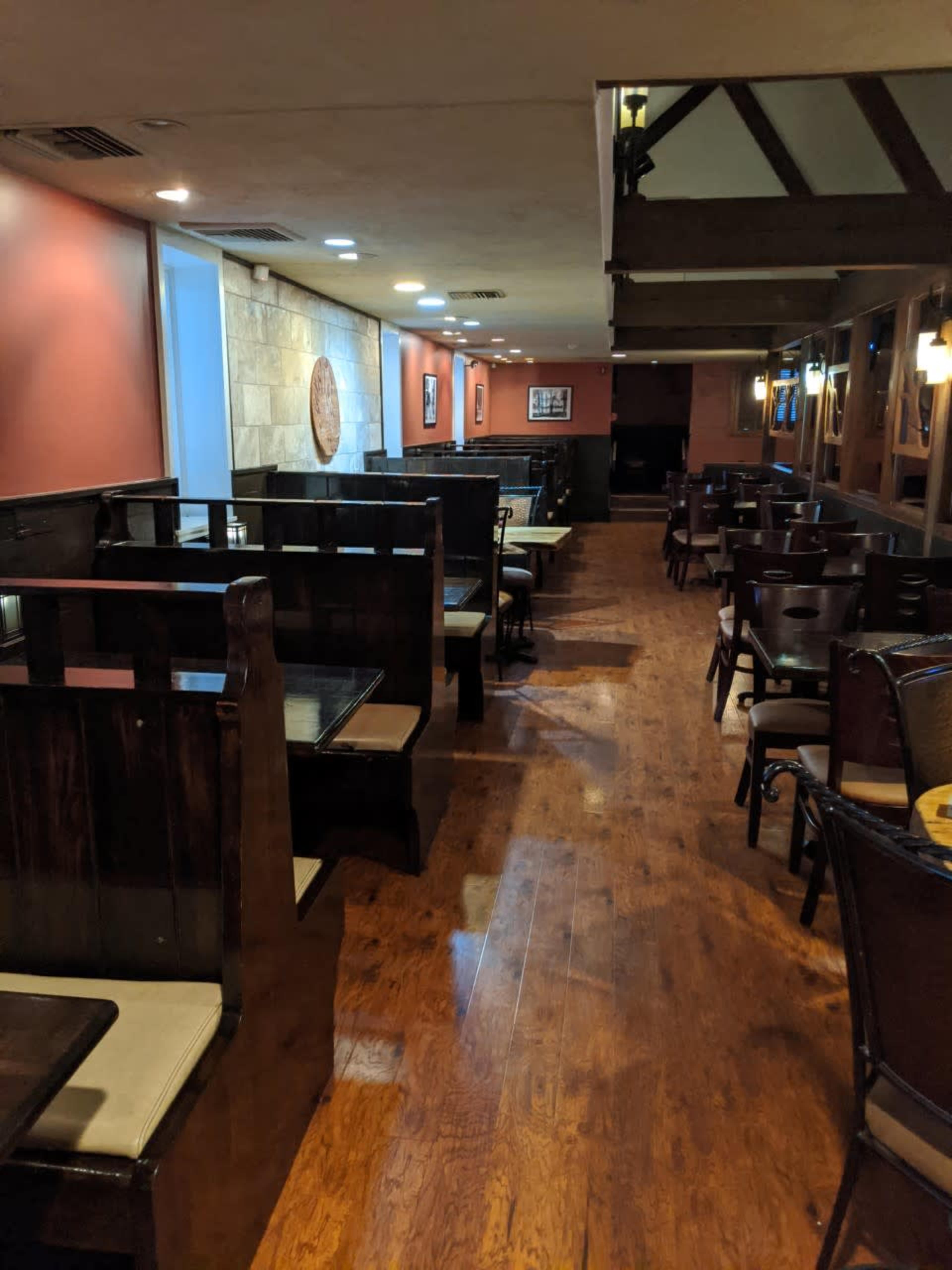 A dimly lit restaurant interior with wooden flooring and booths arranged along the walls.