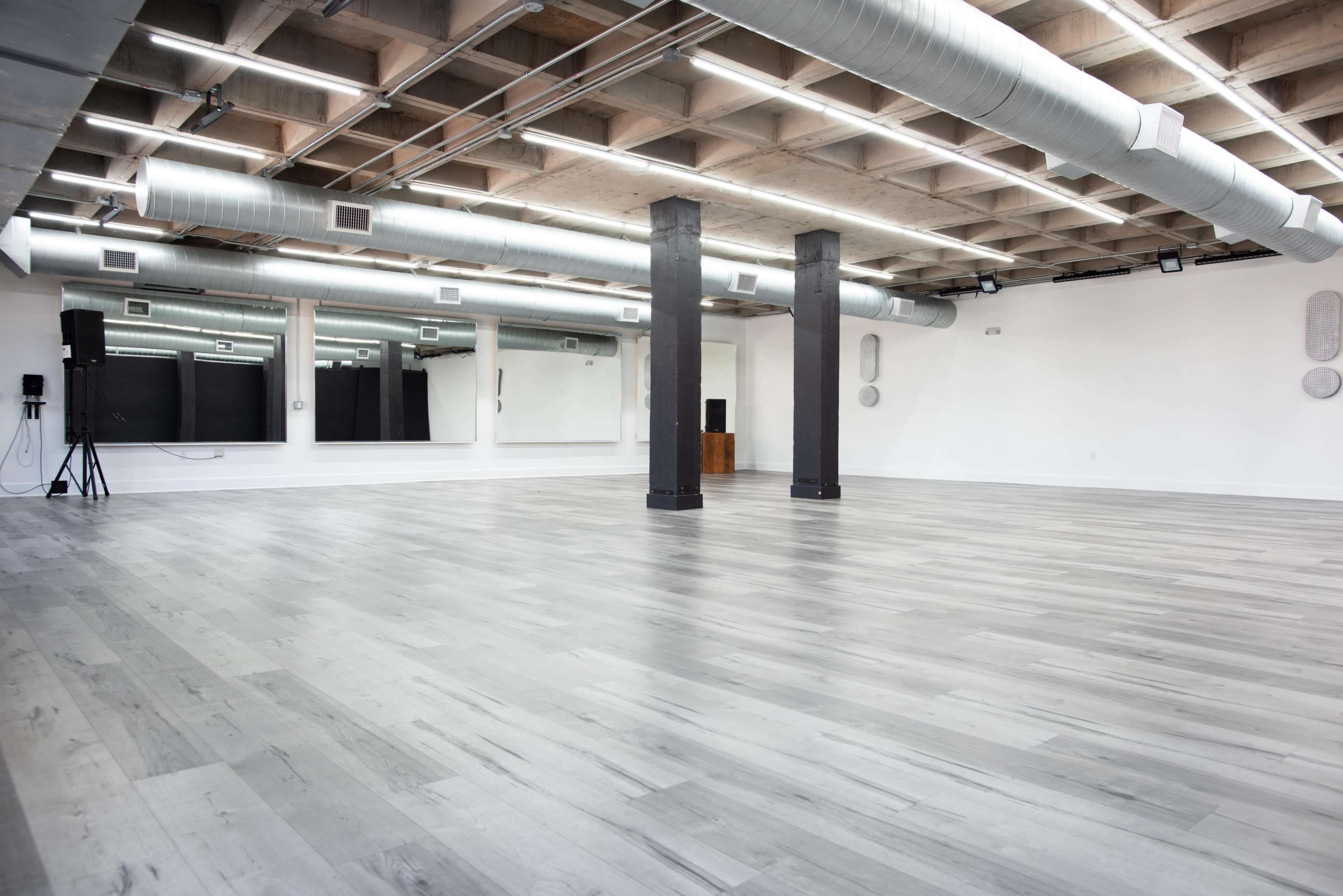 A spacious, bare studio with light-colored wooden flooring and exposed ductwork along the ceiling.