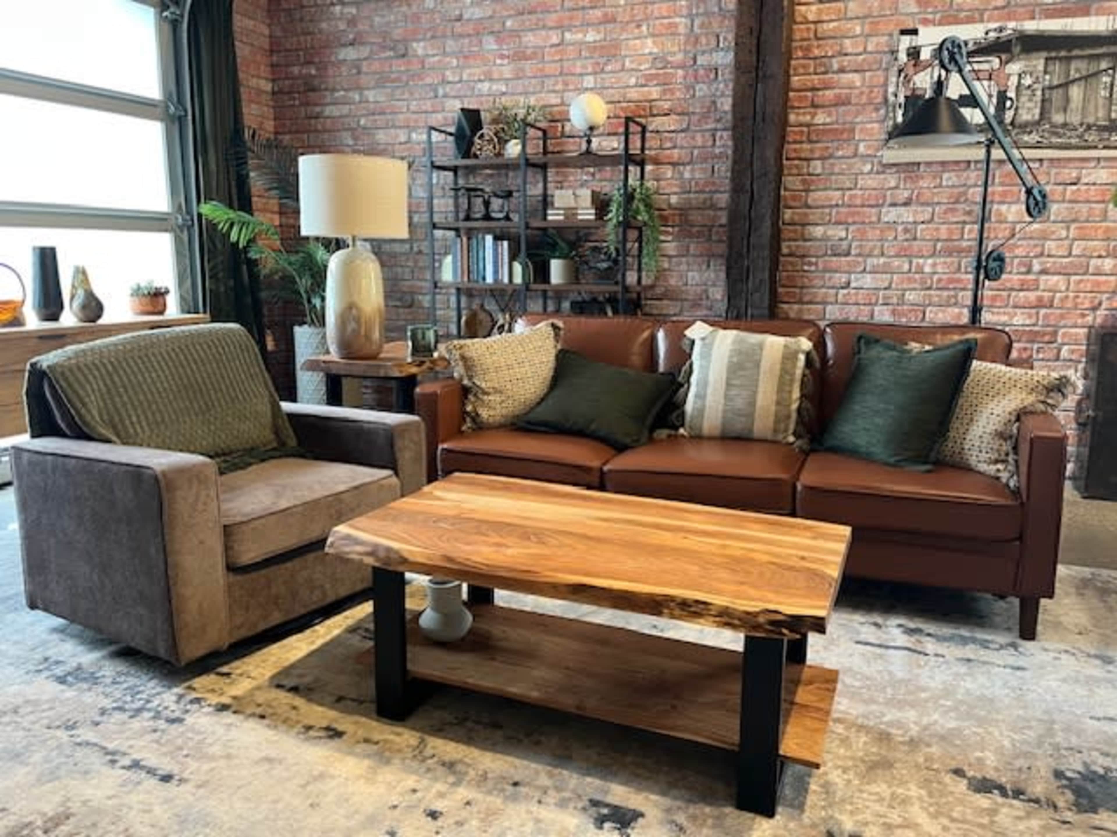 The image shows a cozy living room with a brown leather sofa, an armchair, a wooden coffee table, and exposed brick walls.