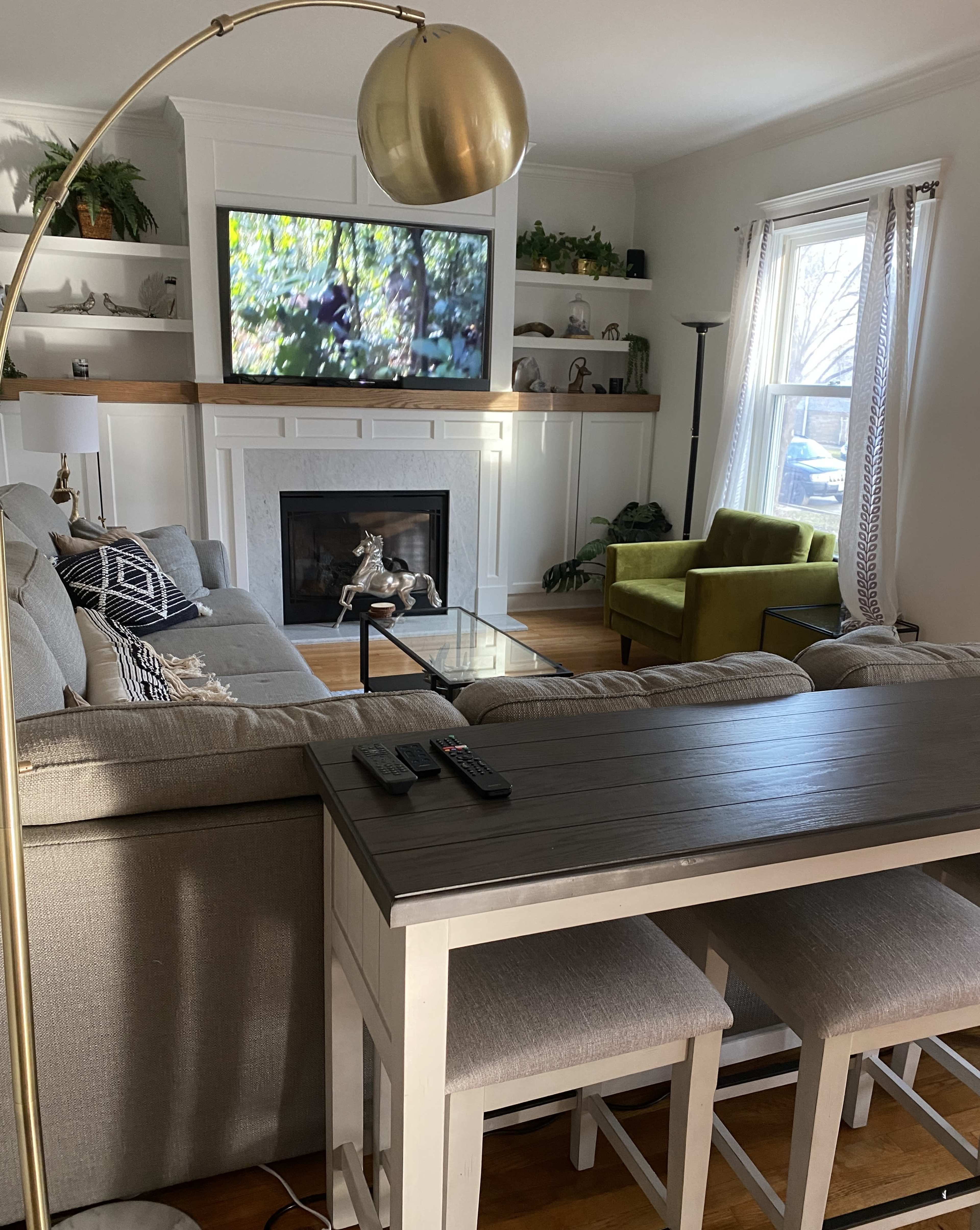 A living room with a gray sofa, a glass coffee table, a flat-screen TV mounted above a white fireplace, and a vibrant green armchair.