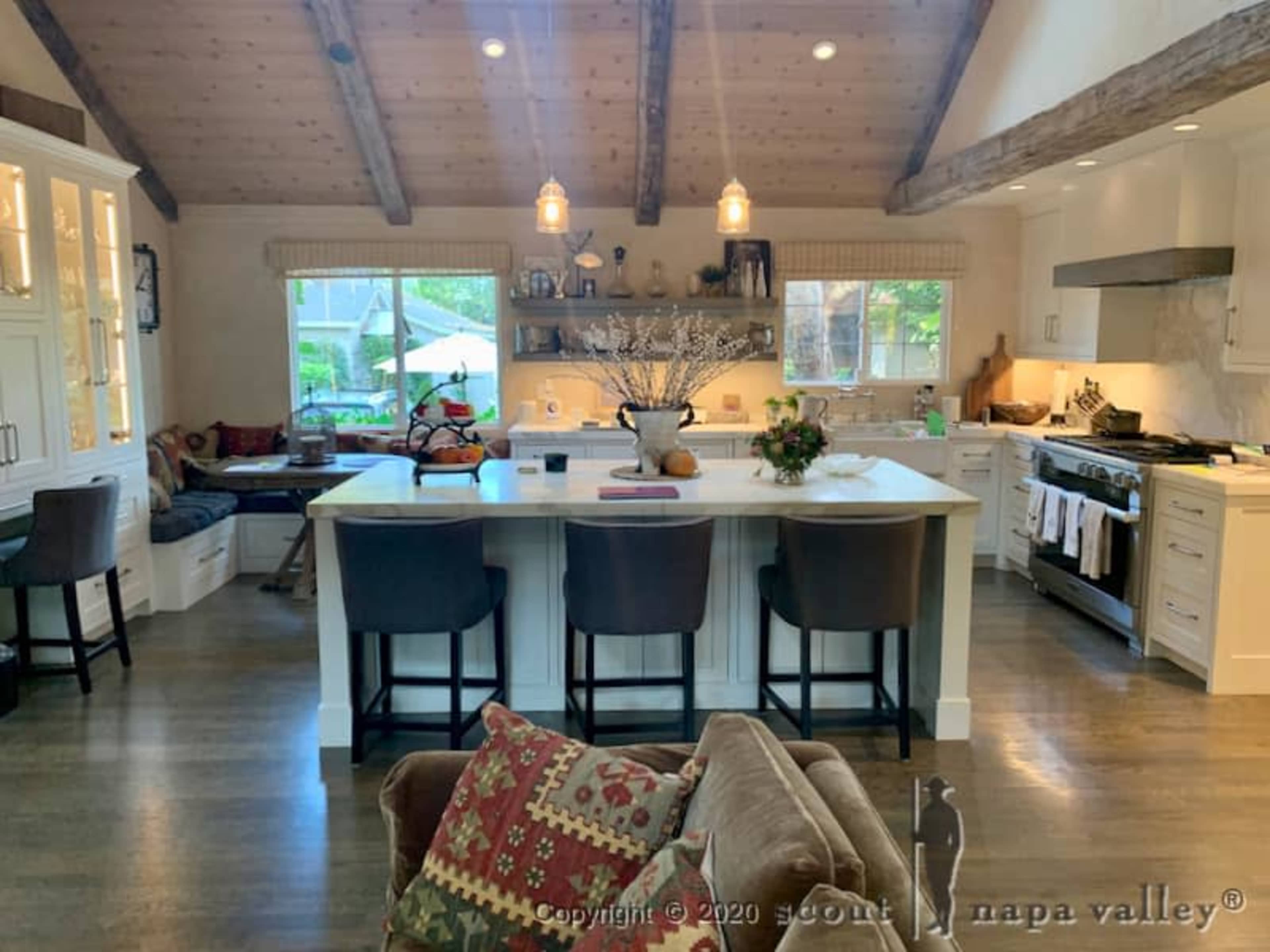 A spacious kitchen with wooden beams, a large island with seating, and a cozy seating area next to a window.