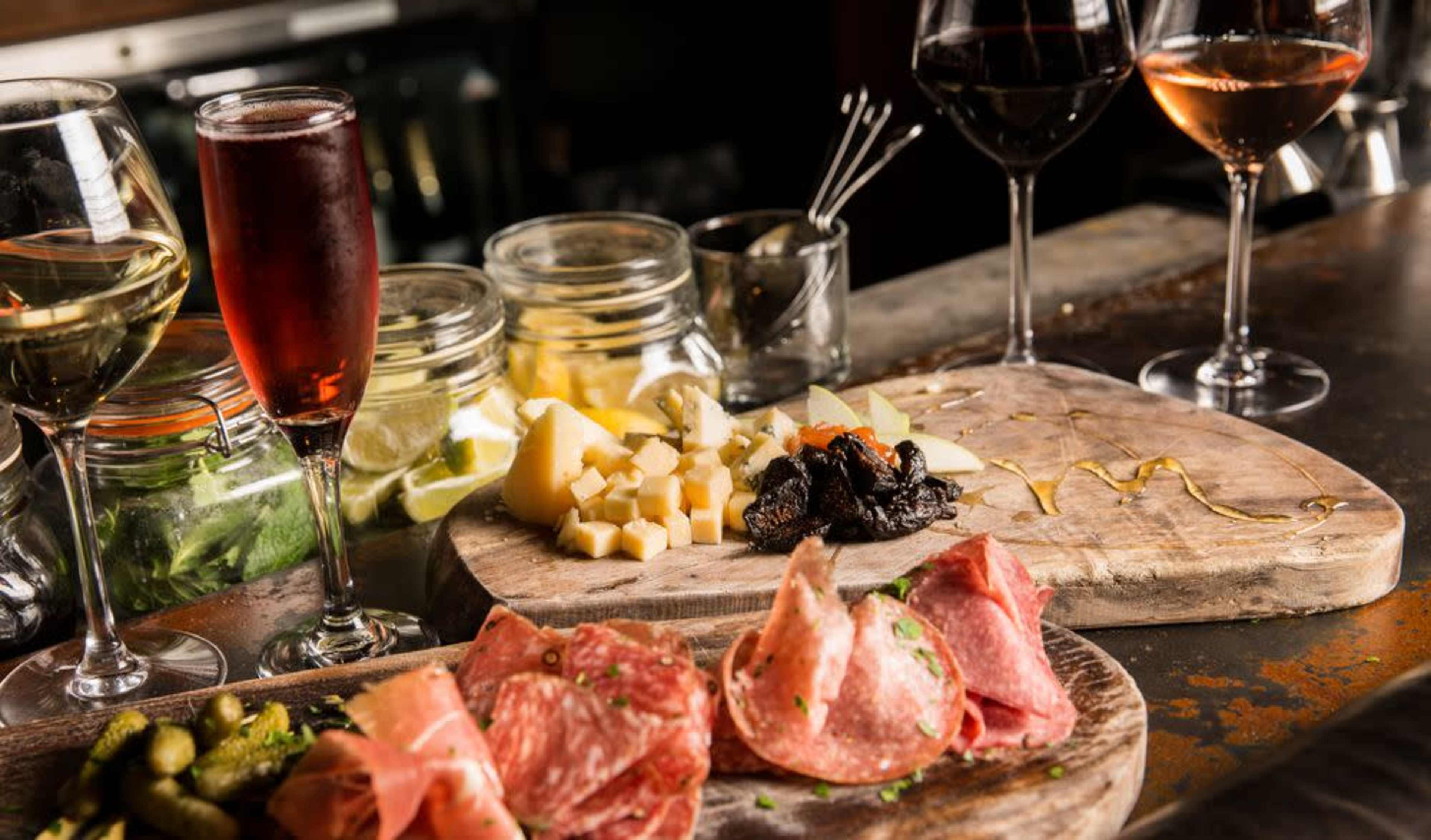 The image showcases a rustic wooden table adorned with various cheeses, cured meats, olives, and several glasses of wine.