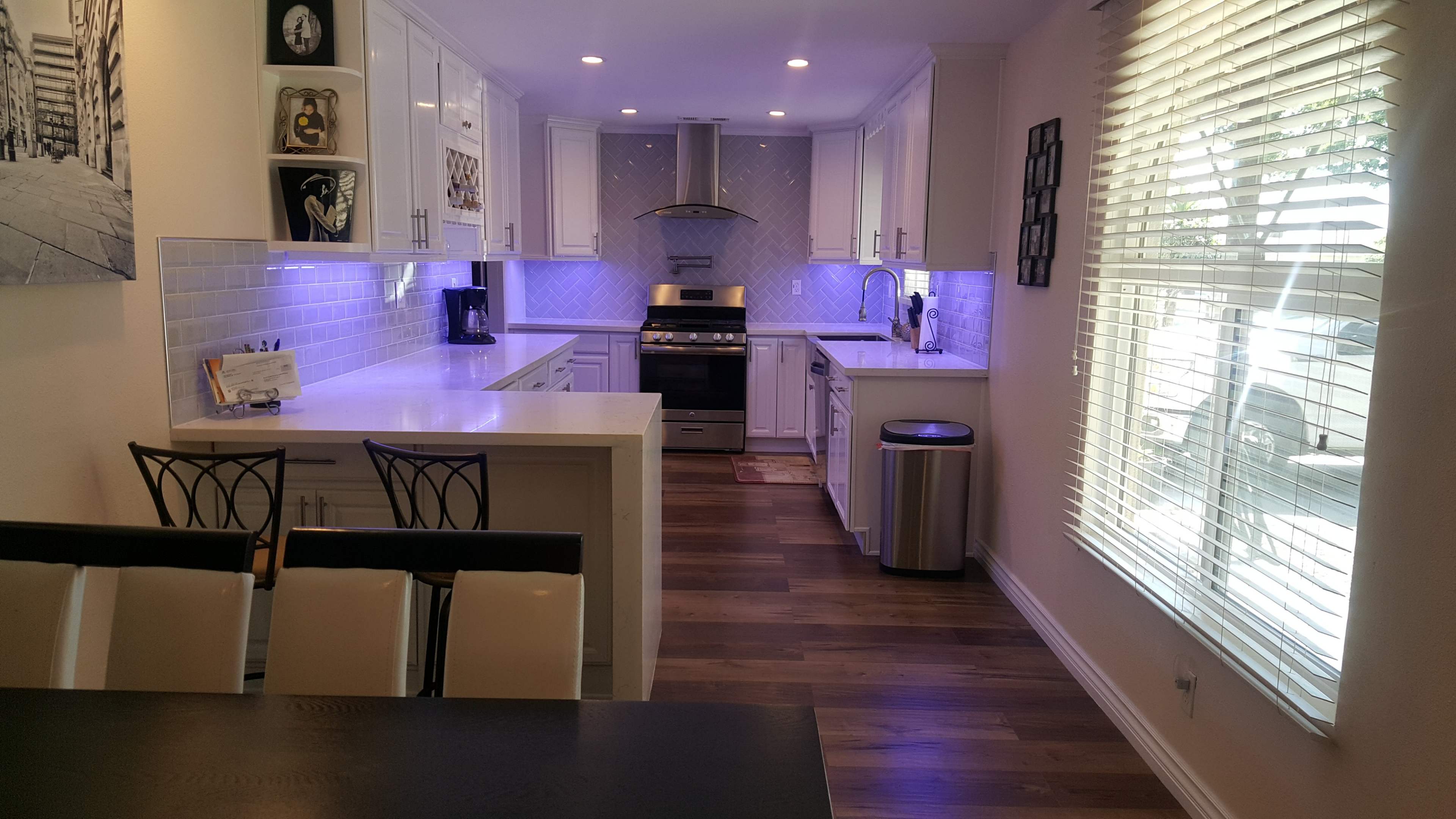 A modern kitchen features white cabinetry, a stainless steel gas stove, and ambient lighting beneath the cabinets.