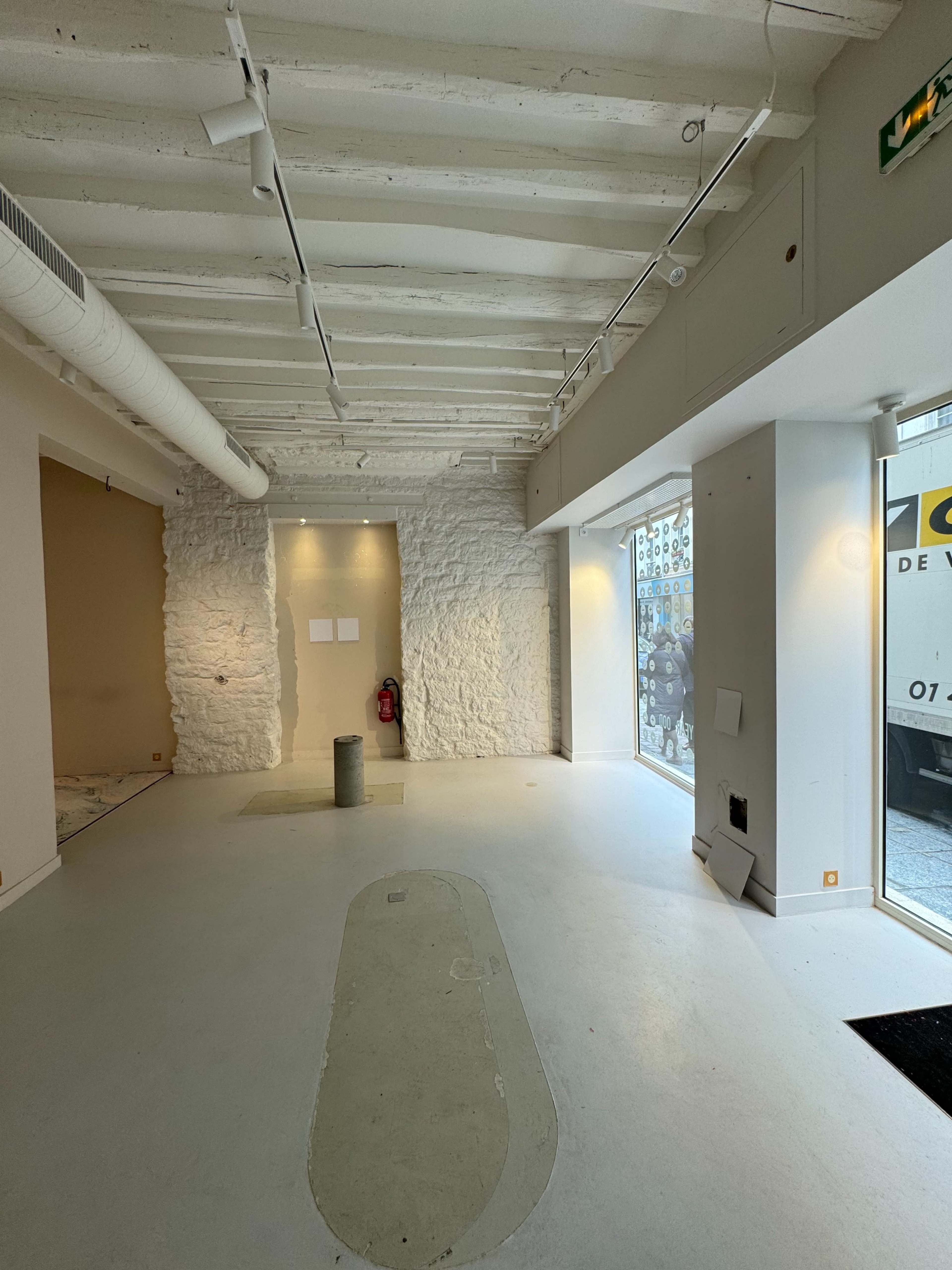 An empty commercial space with white walls, exposed ceiling beams, and large windows facing the street.