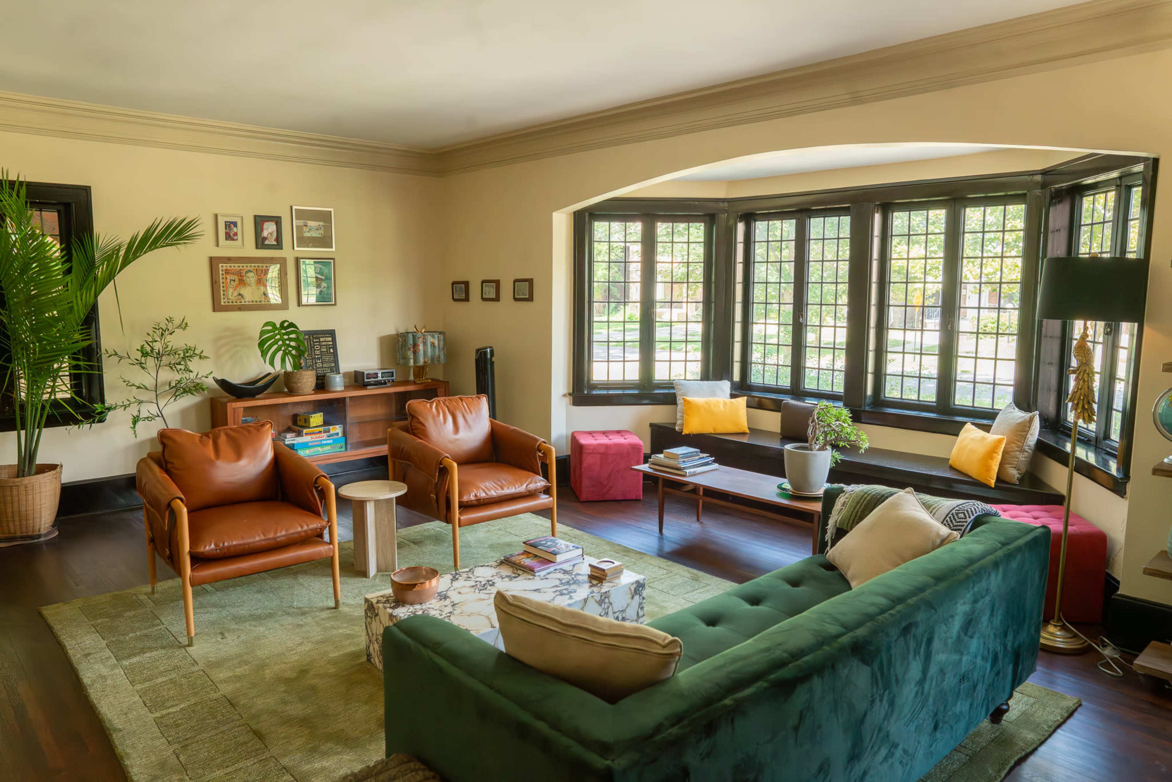 The image shows a cozy living room featuring two leather armchairs, a green sofa, a coffee table, and large windows with a view of the outdoors.