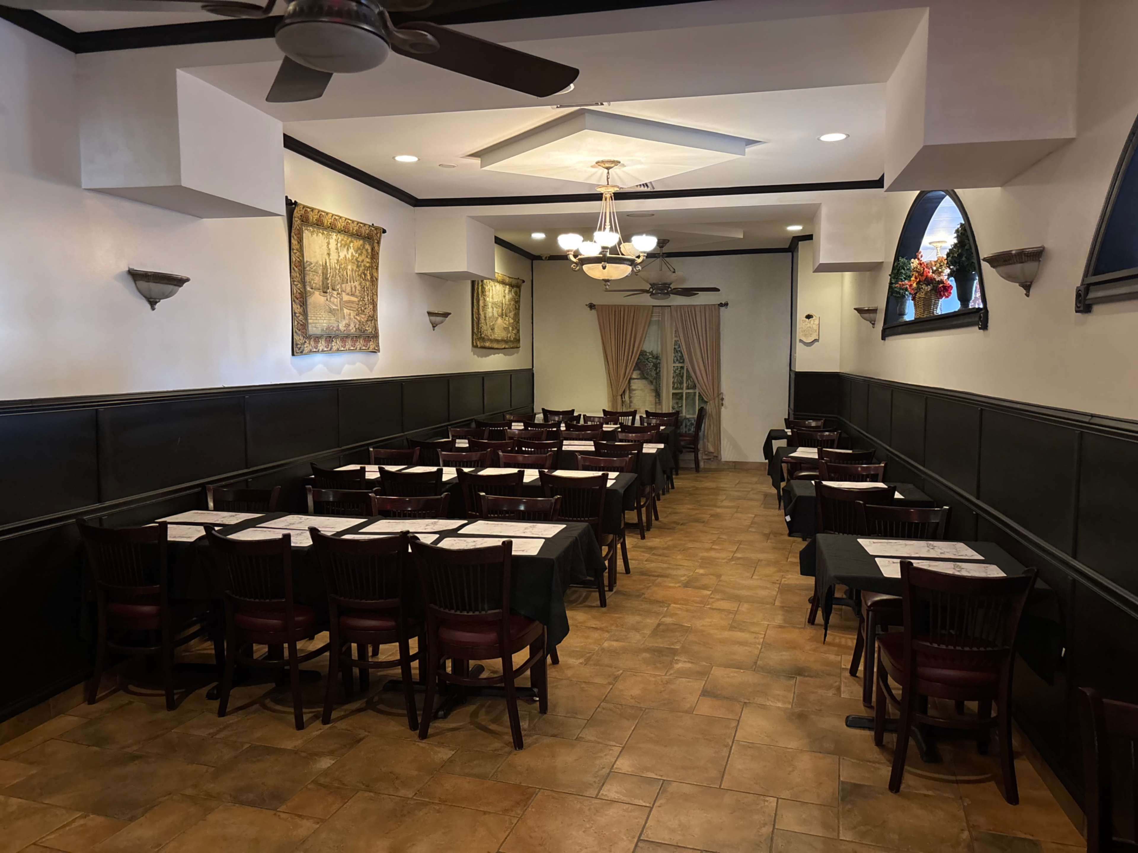 The image shows a spacious restaurant interior featuring tables set for dining, with decorative wall art and lighting fixtures.
