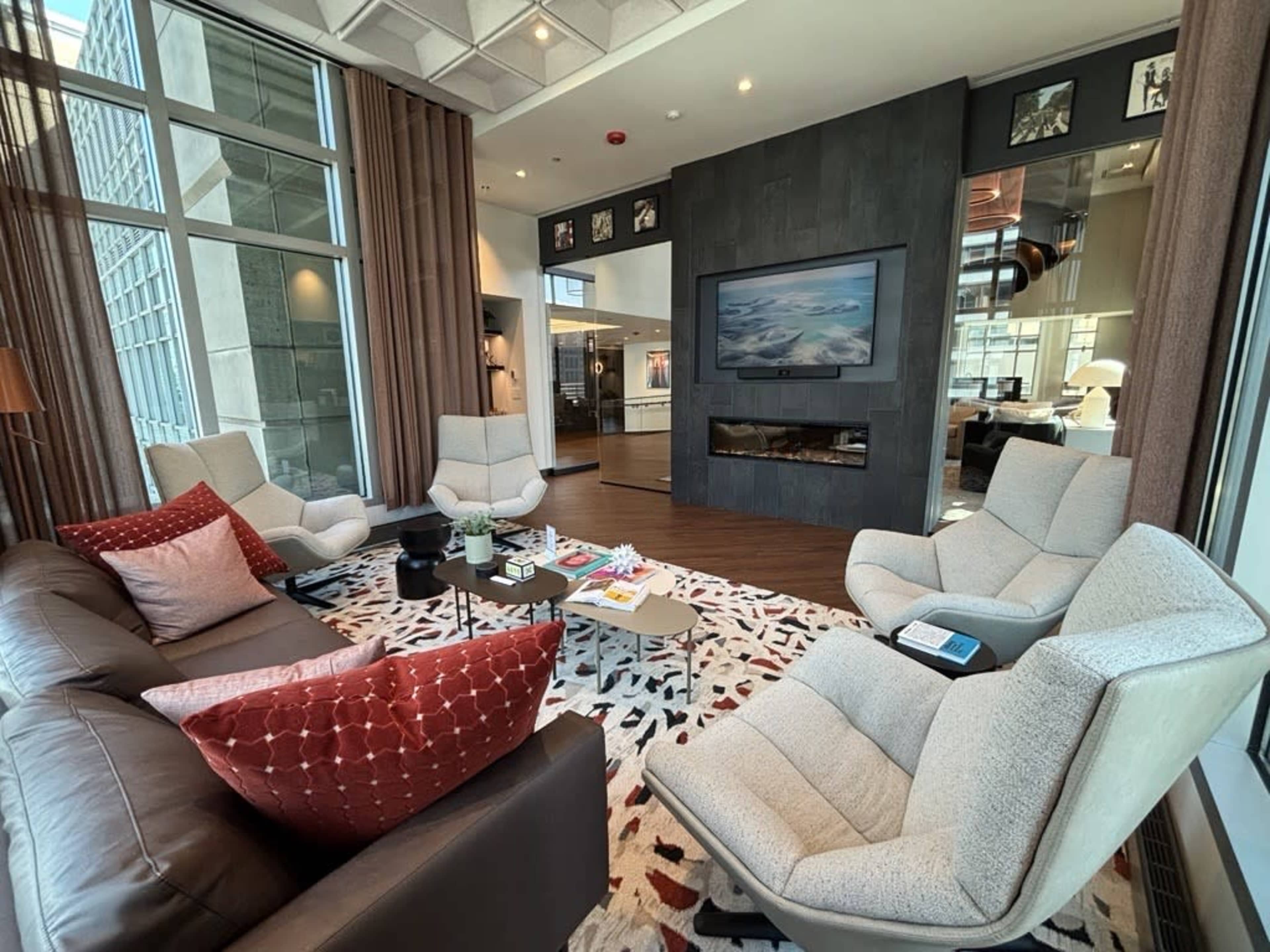 The image shows a modern living room with multiple seating areas, a fireplace, large windows, and decorative elements such as a rug and various cushions.