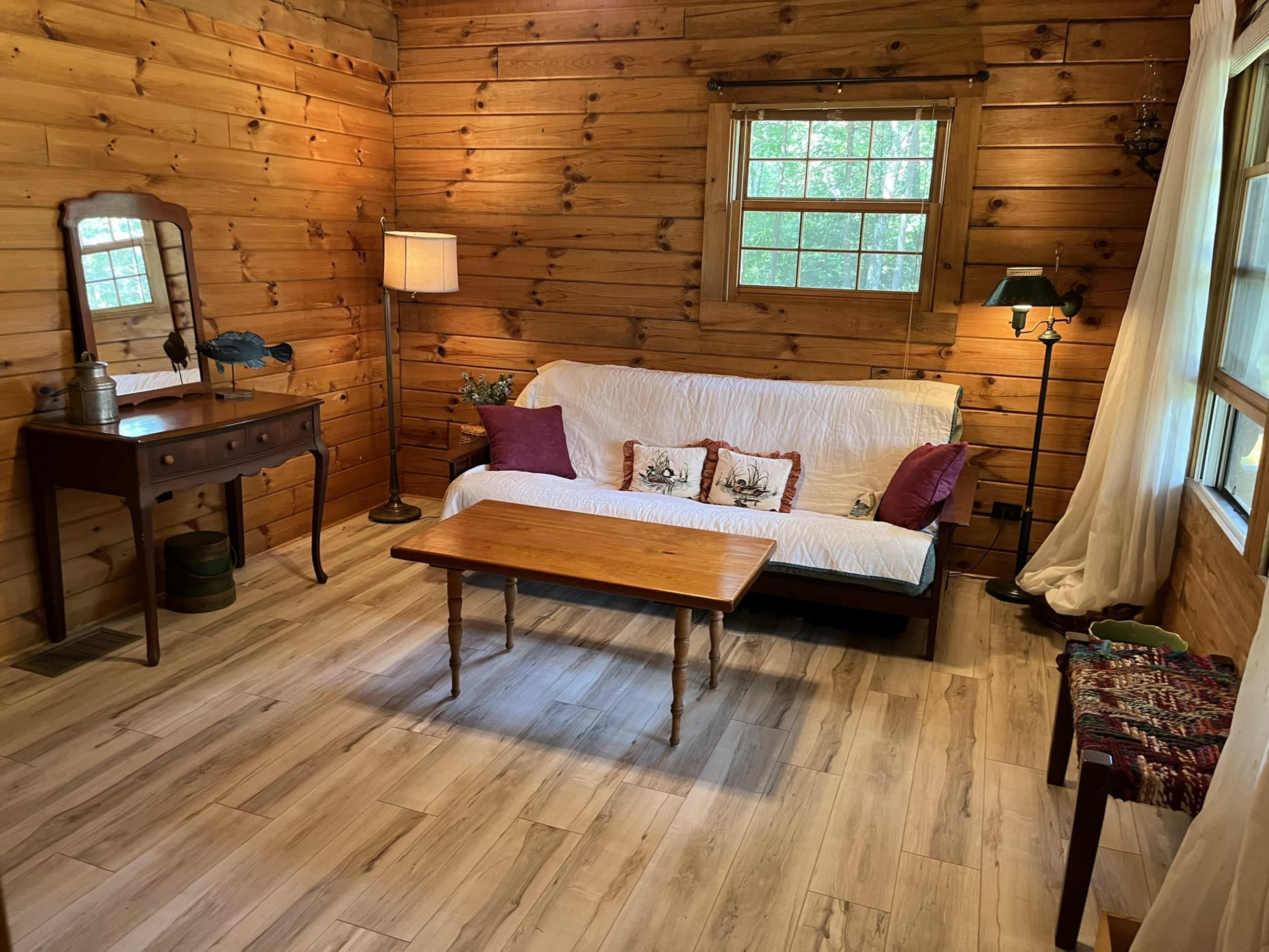 A cozy wooden room with a sofa, a coffee table, a lamp, and a mirror against the walls.