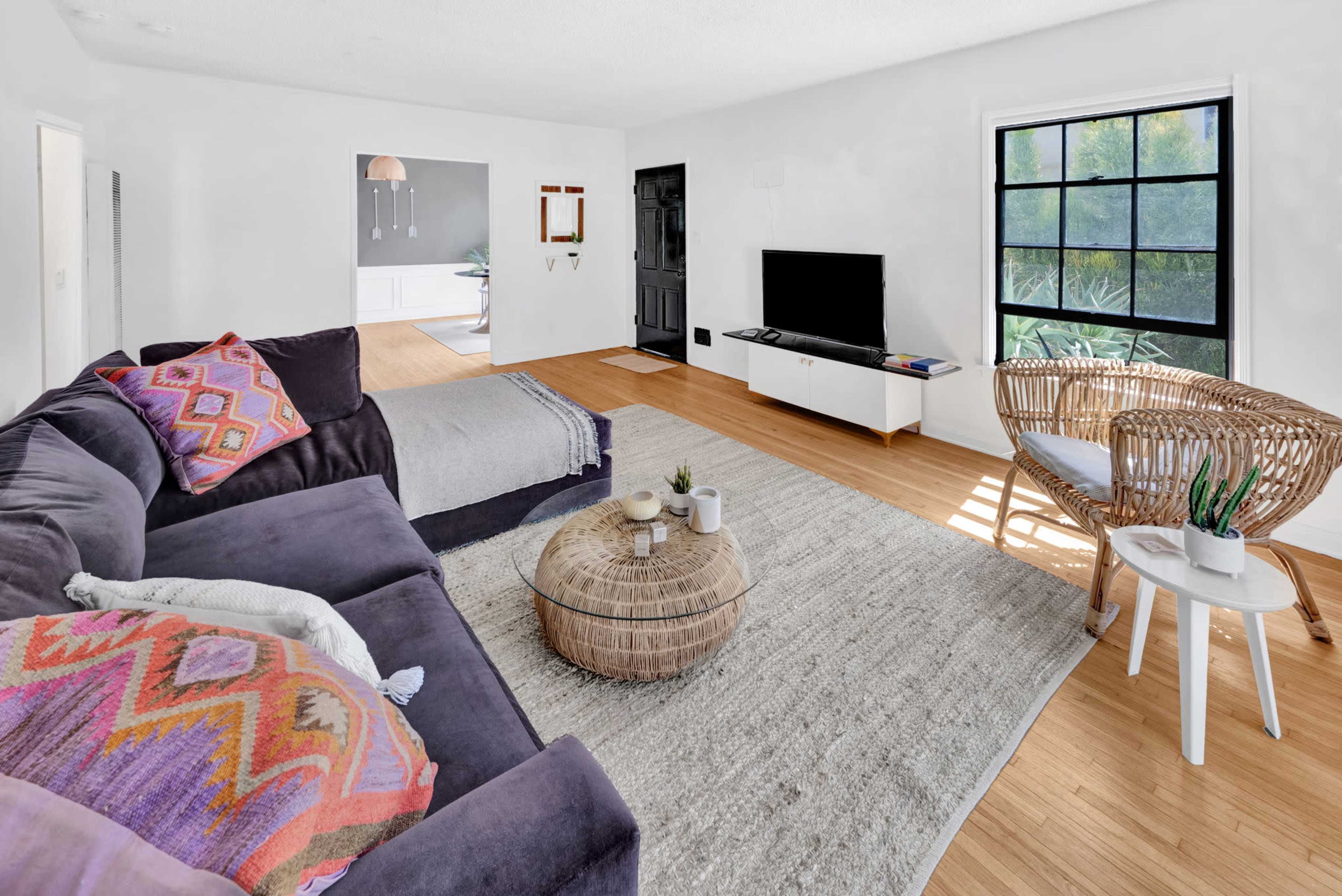 A modern living room features a dark sofa, a round coffee table, and a large window overlooking greenery.