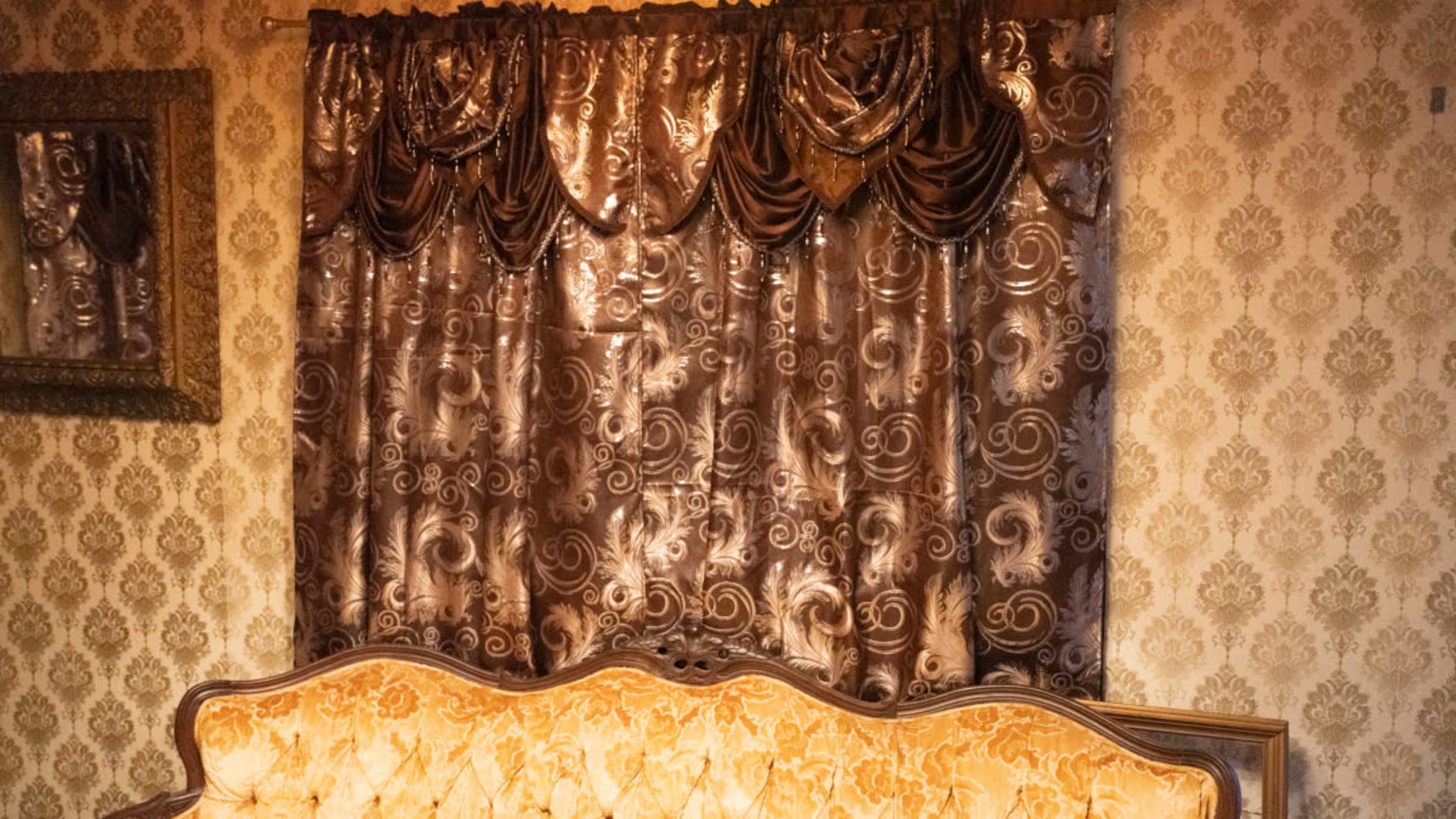 The image features a vintage room with patterned wallpaper and ornate curtains above a tufted, golden couch.