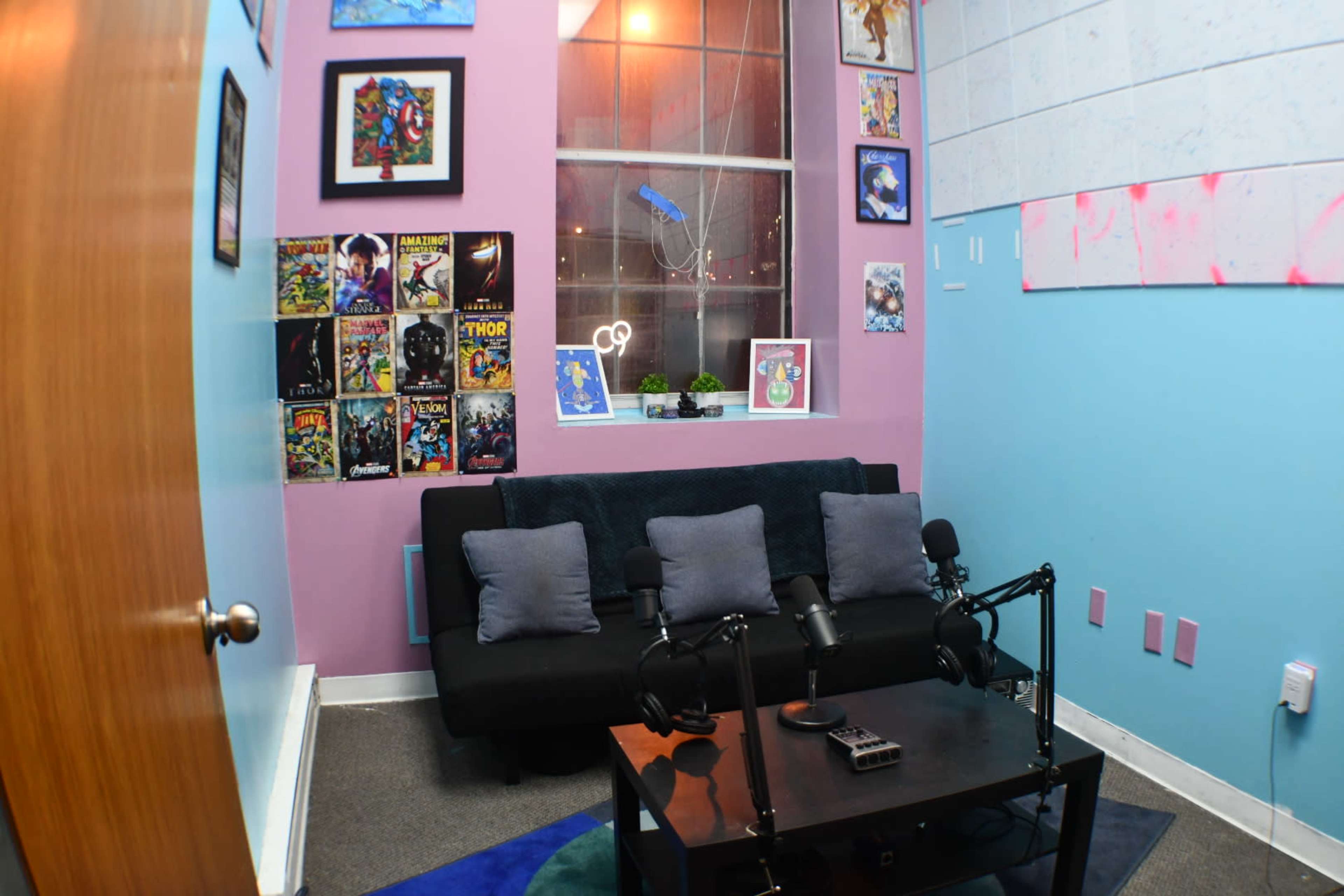A small room with a sofa, two microphones on a table, and walls adorned with comic book art and posters.