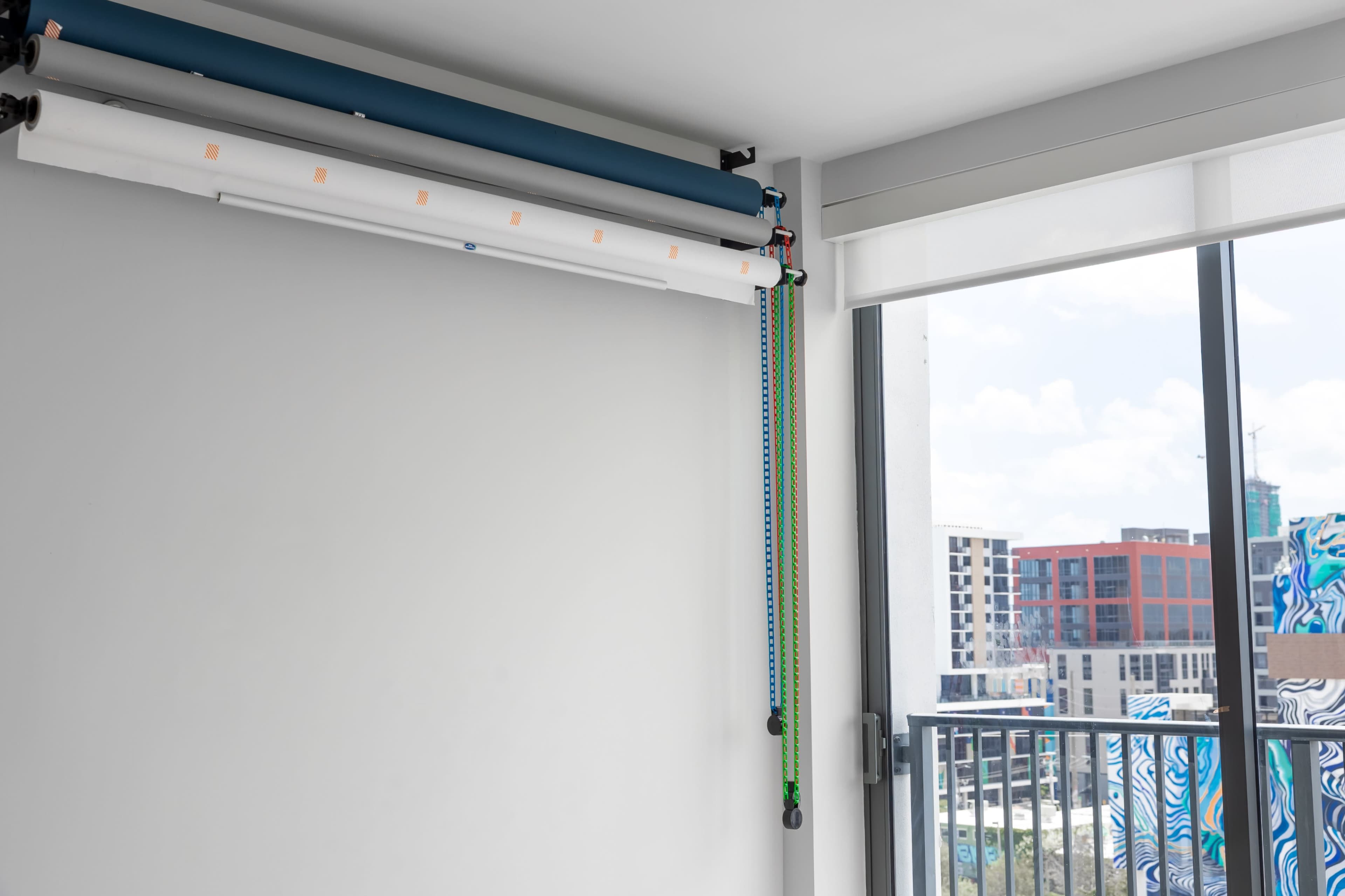 The image shows a roll-up backdrop system mounted on a wall next to a window with a view of a cityscape.