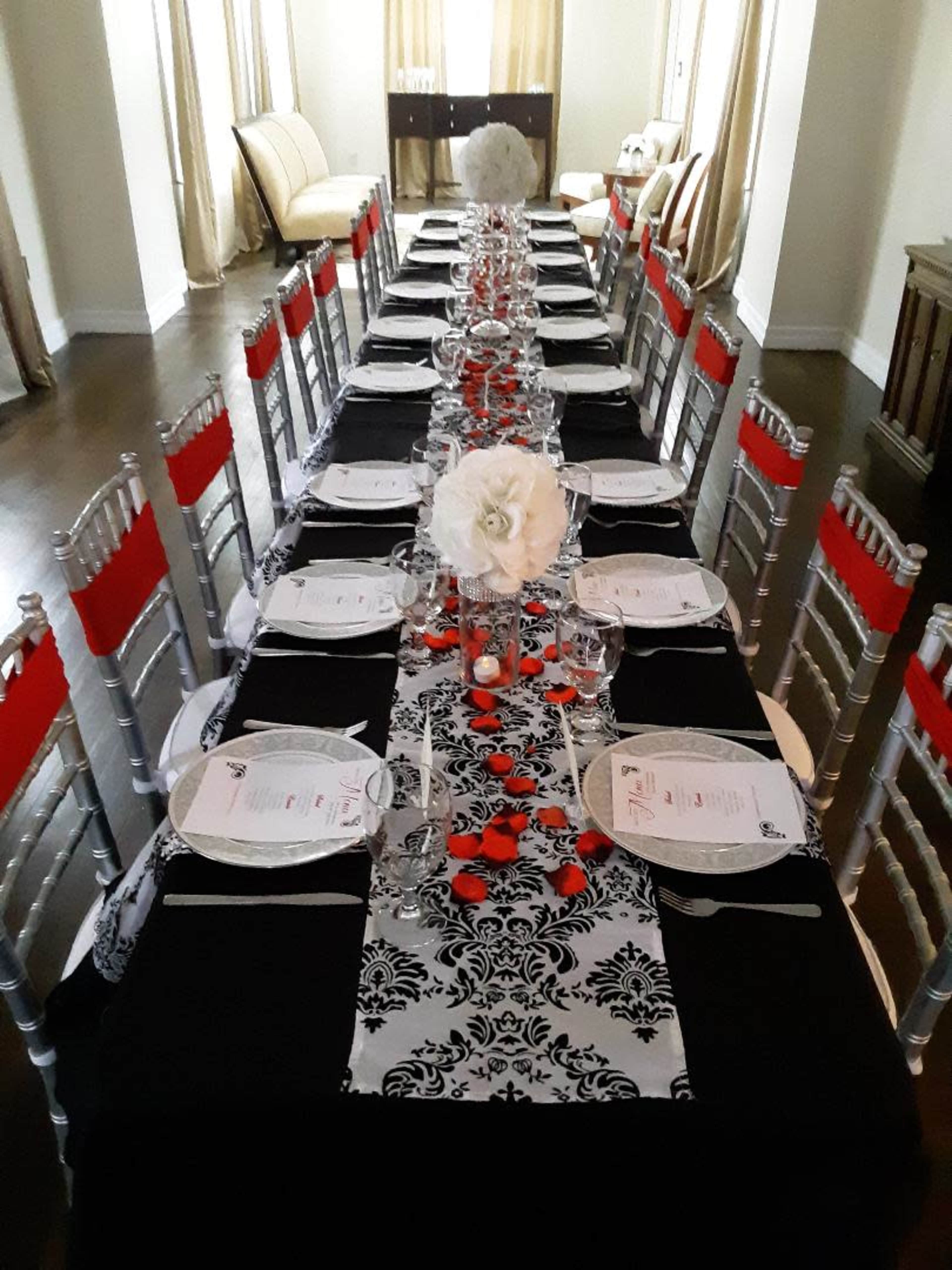 A long dining table is set with black and white tablecloths, red accents, plates, glasses, and floral centerpieces.