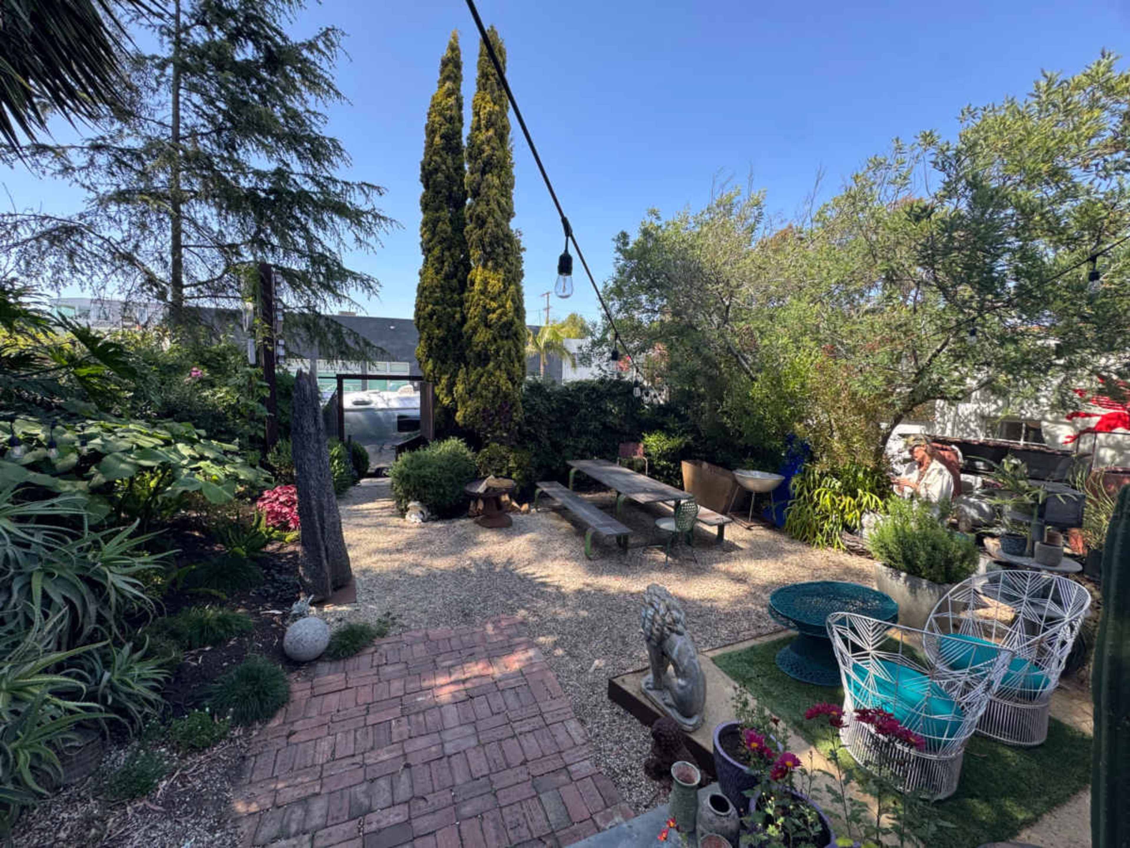 The image shows a landscaped garden featuring a gravel area with seating, various plants, and a few decorative elements.