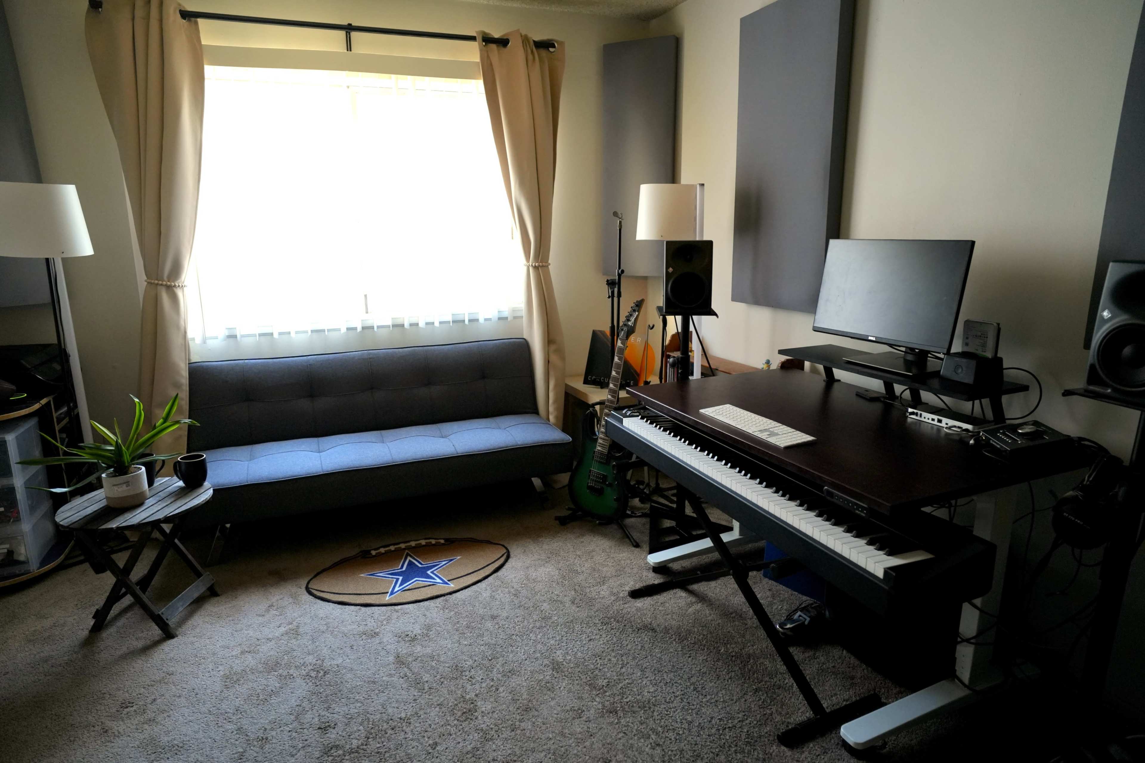 The image shows a music recording studio with a keyboard, speakers, a computer monitor, a sofa, and a small table, all arranged around a window with light-colored curtains.