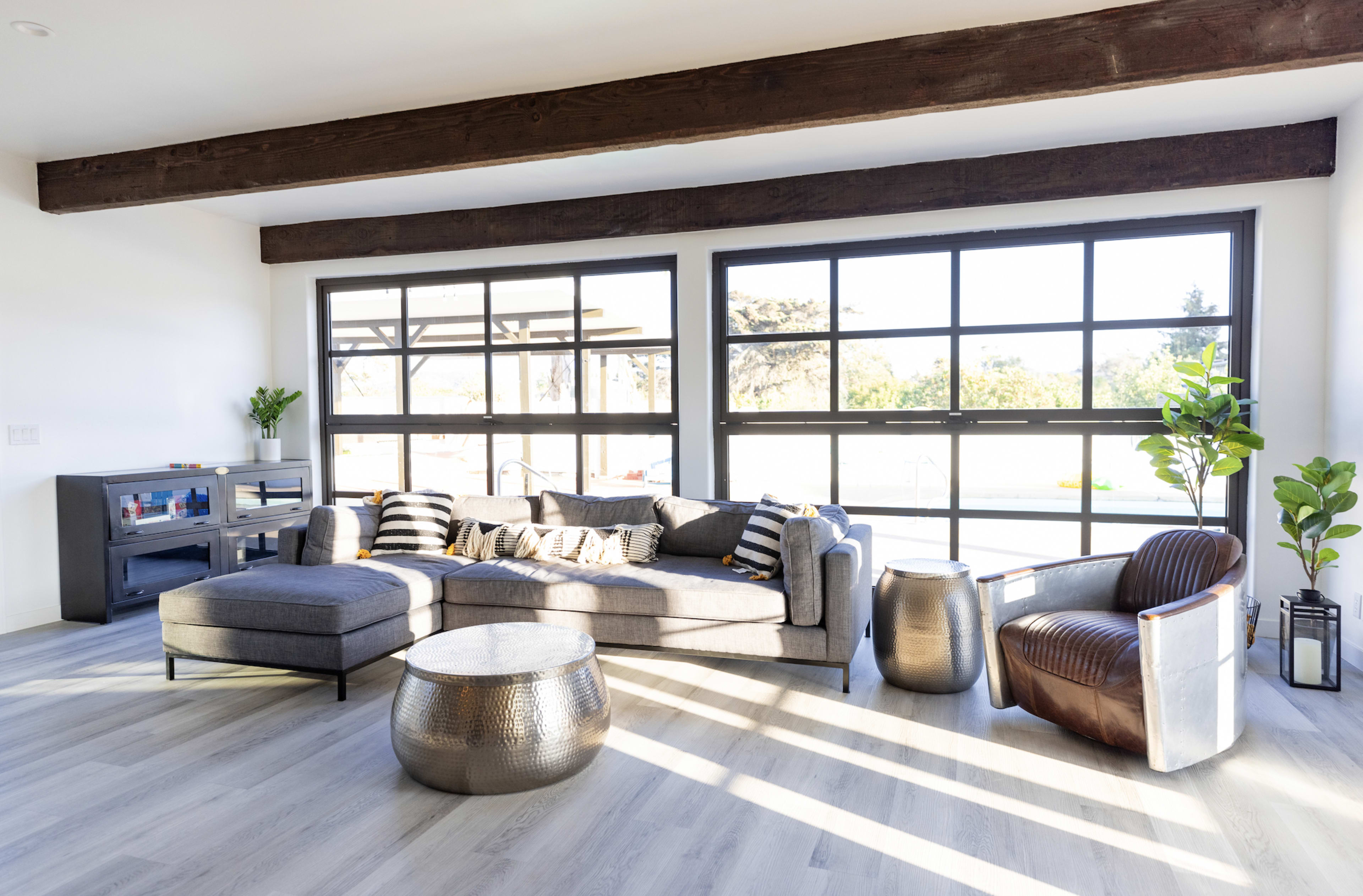 A modern living room features a sectional sofa, a round metallic coffee table, and large windows that allow natural light to illuminate the space.