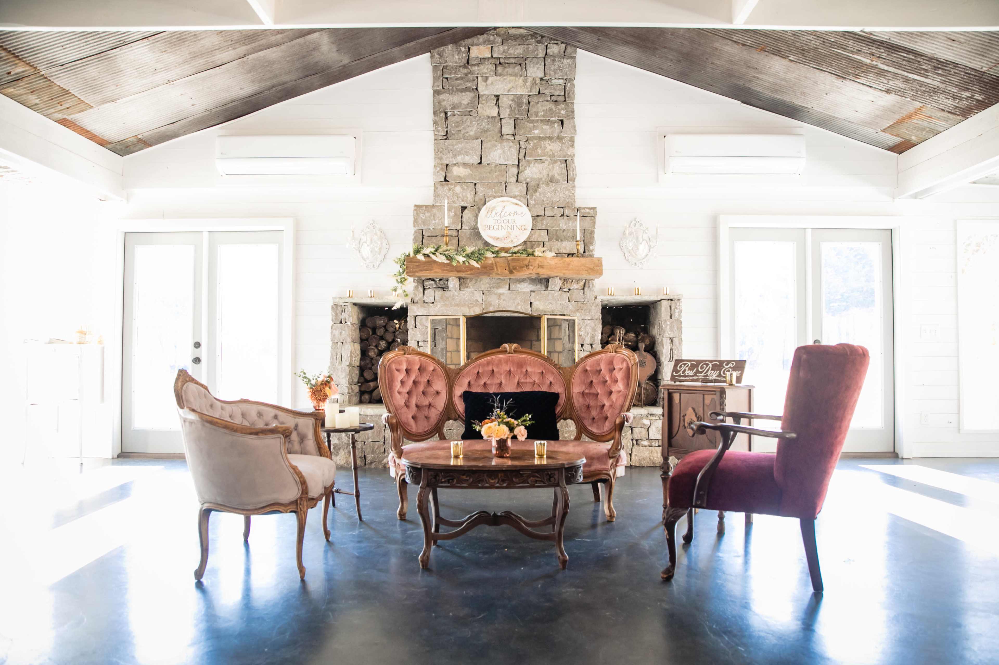 A cozy sitting area features a stone fireplace, a wooden mantel, and various upholstered chairs arranged around a central table.