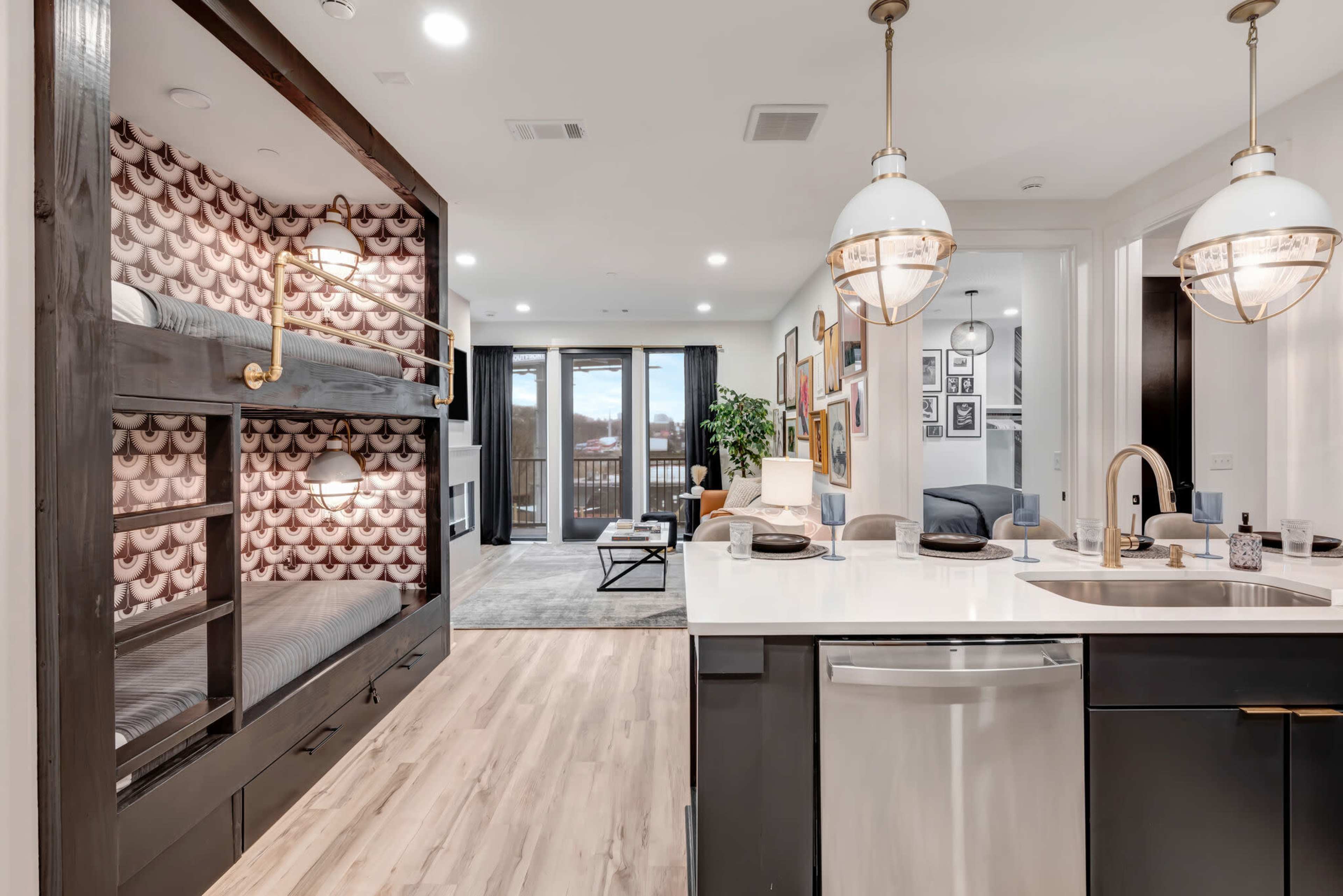 A modern living space featuring a kitchen with an island and a bunk bed area, separated by a decorative wall, leading into a cozy lounge area.