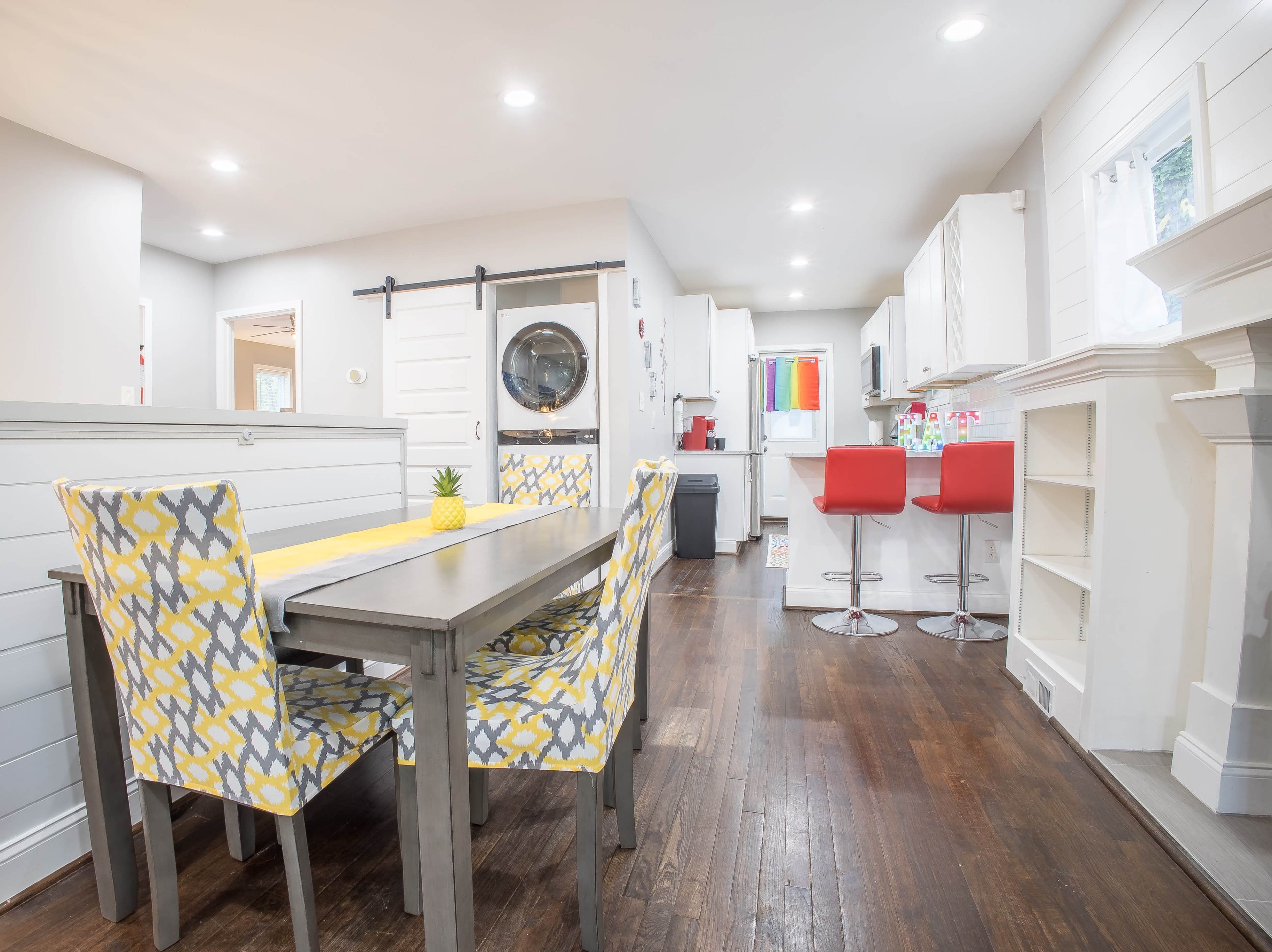 A modern kitchen and dining area featuring a rectangular table with patterned chairs, a circular wall-mounted mirror, and a bright, open layout.