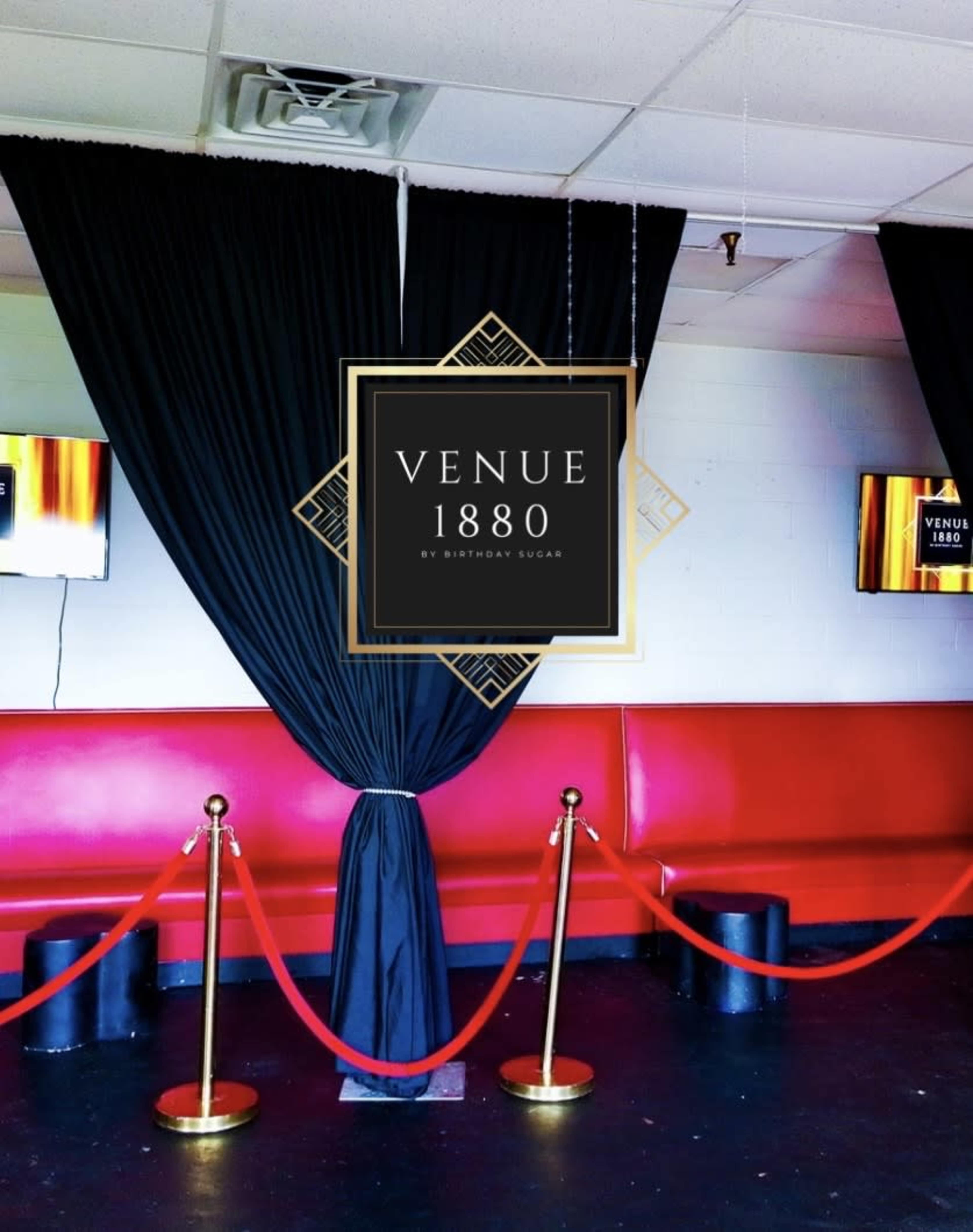 The image shows a lounge area with red seating, black curtains, and a decorative sign for "Venue 1880" by Birthday Sugar.
