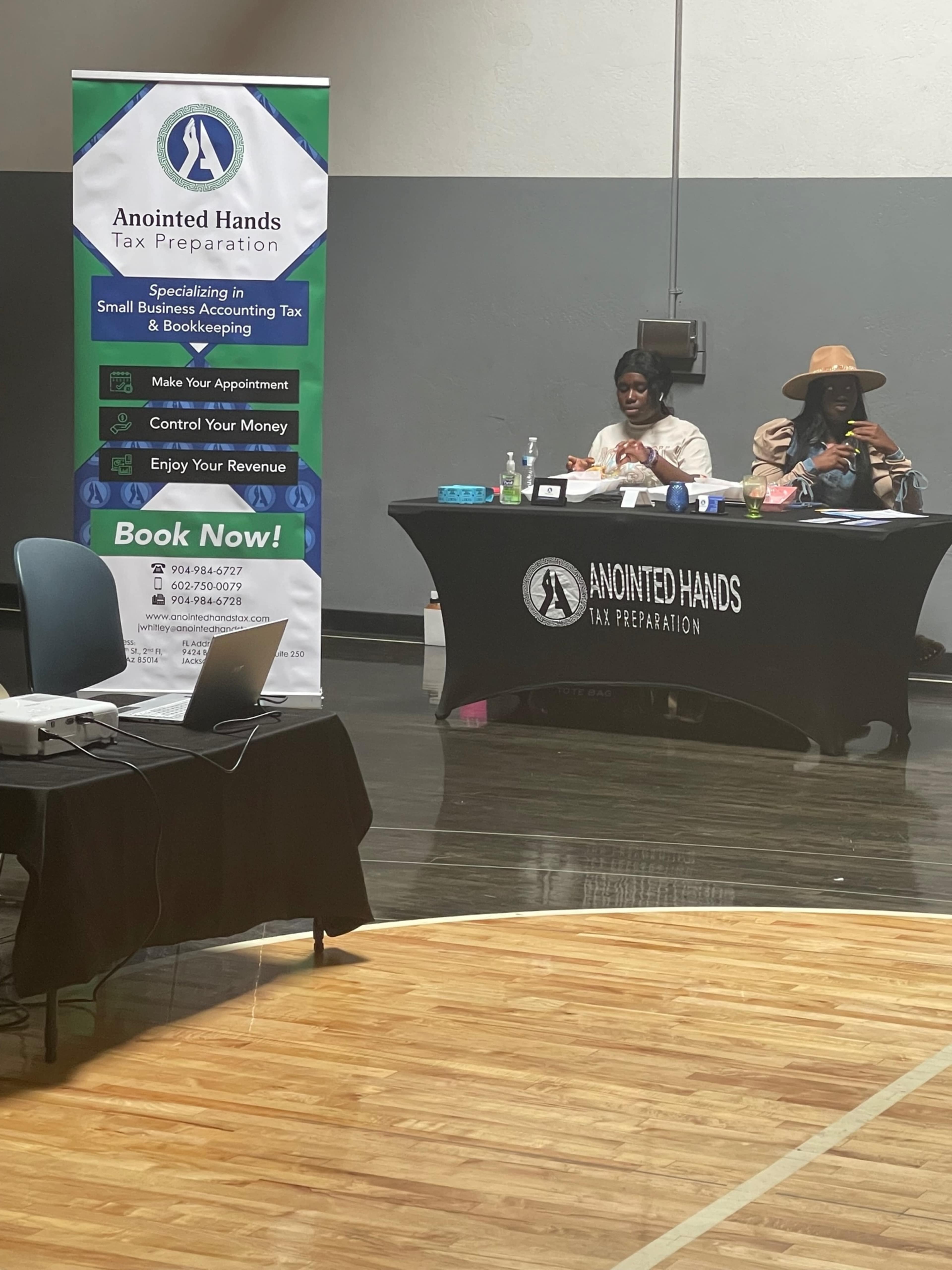 A tax preparation booth set up with a banner and table displaying services, while two individuals sit at the table.