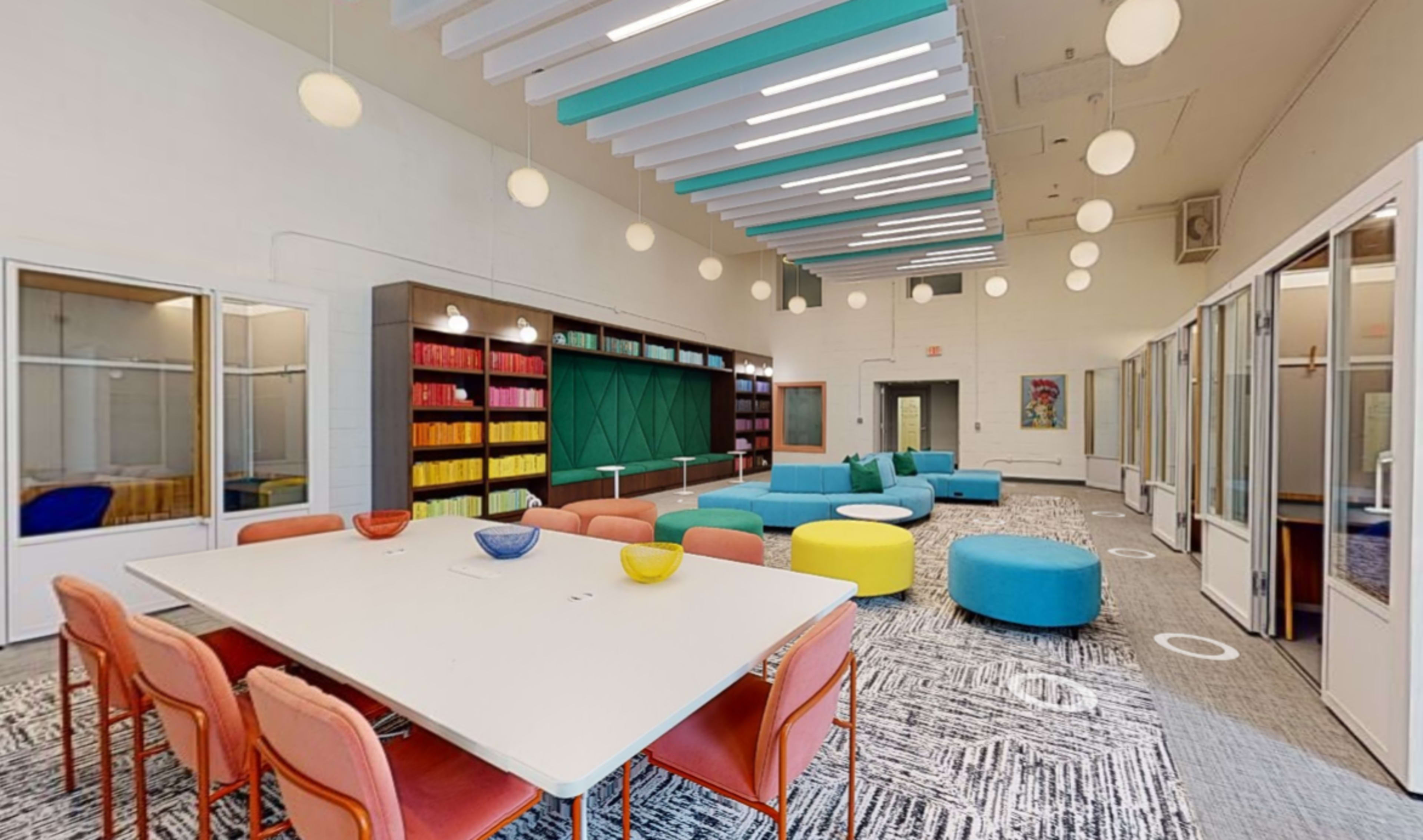 A brightly colored communal space with a large table surrounded by chairs, soft seating areas, and shelves filled with vibrant organizational boxes.