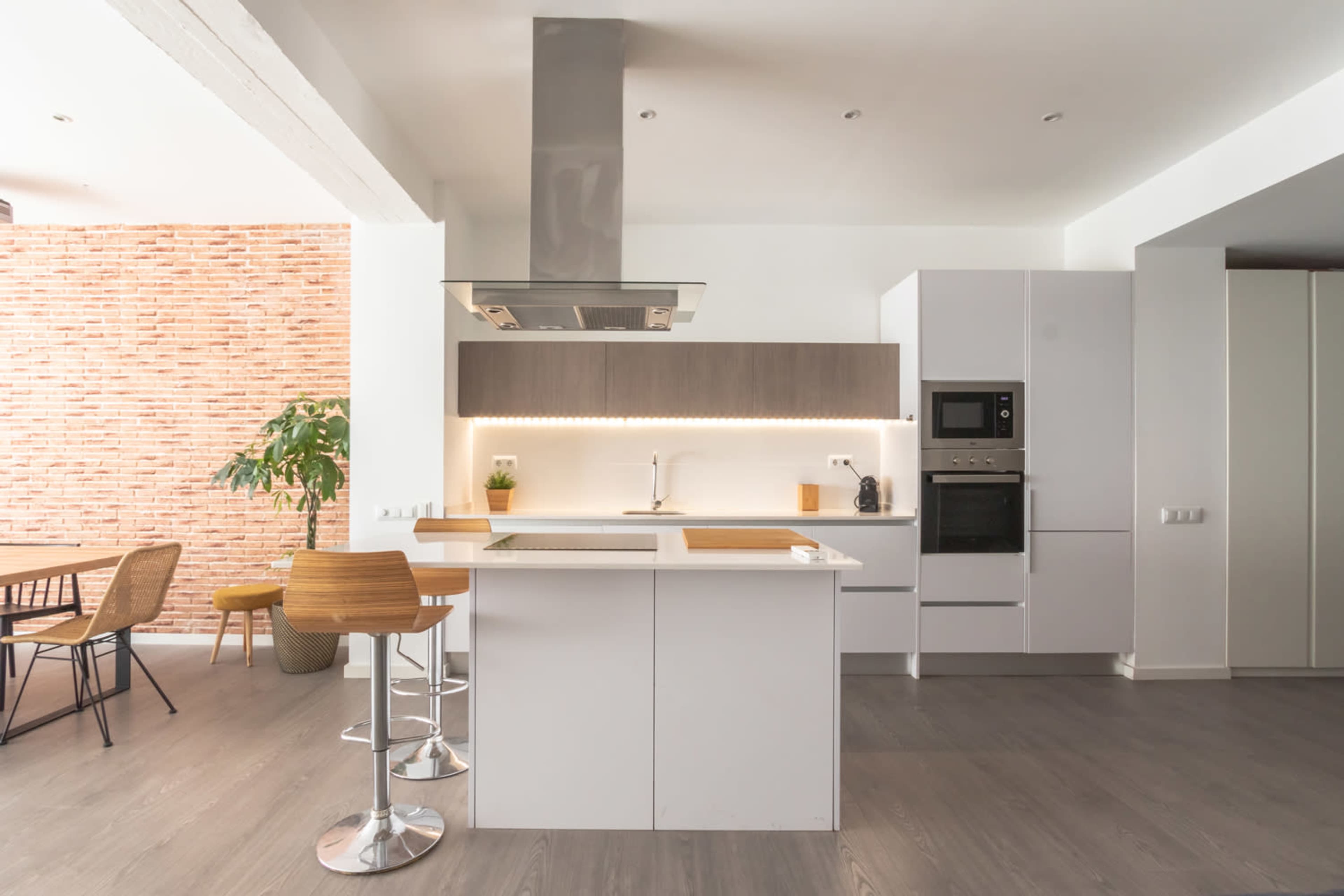 The image shows a modern kitchen with a central island, stainless steel appliances, and a brick accent wall.
