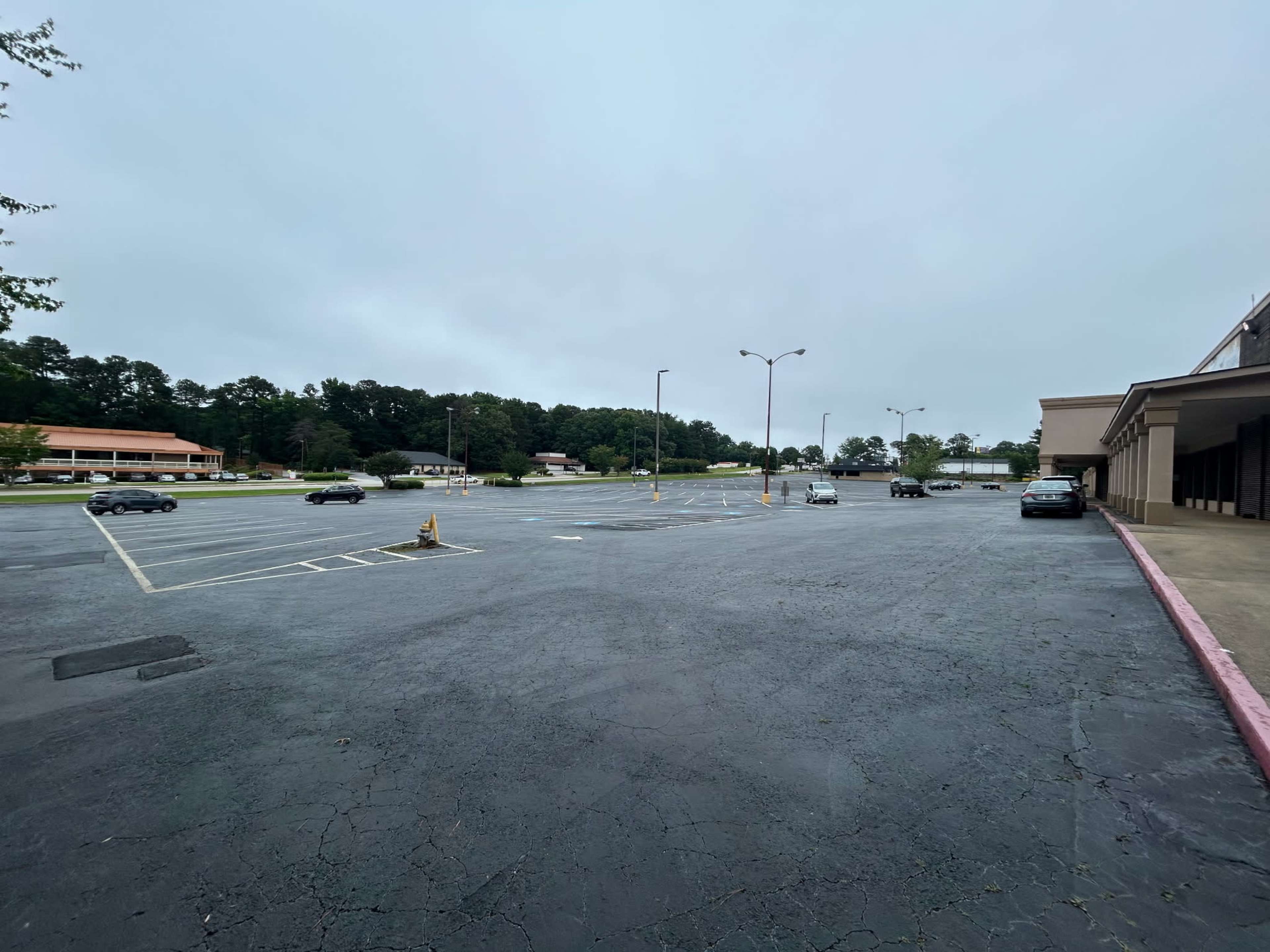 An empty parking lot with several parked cars and overcast skies in the background.