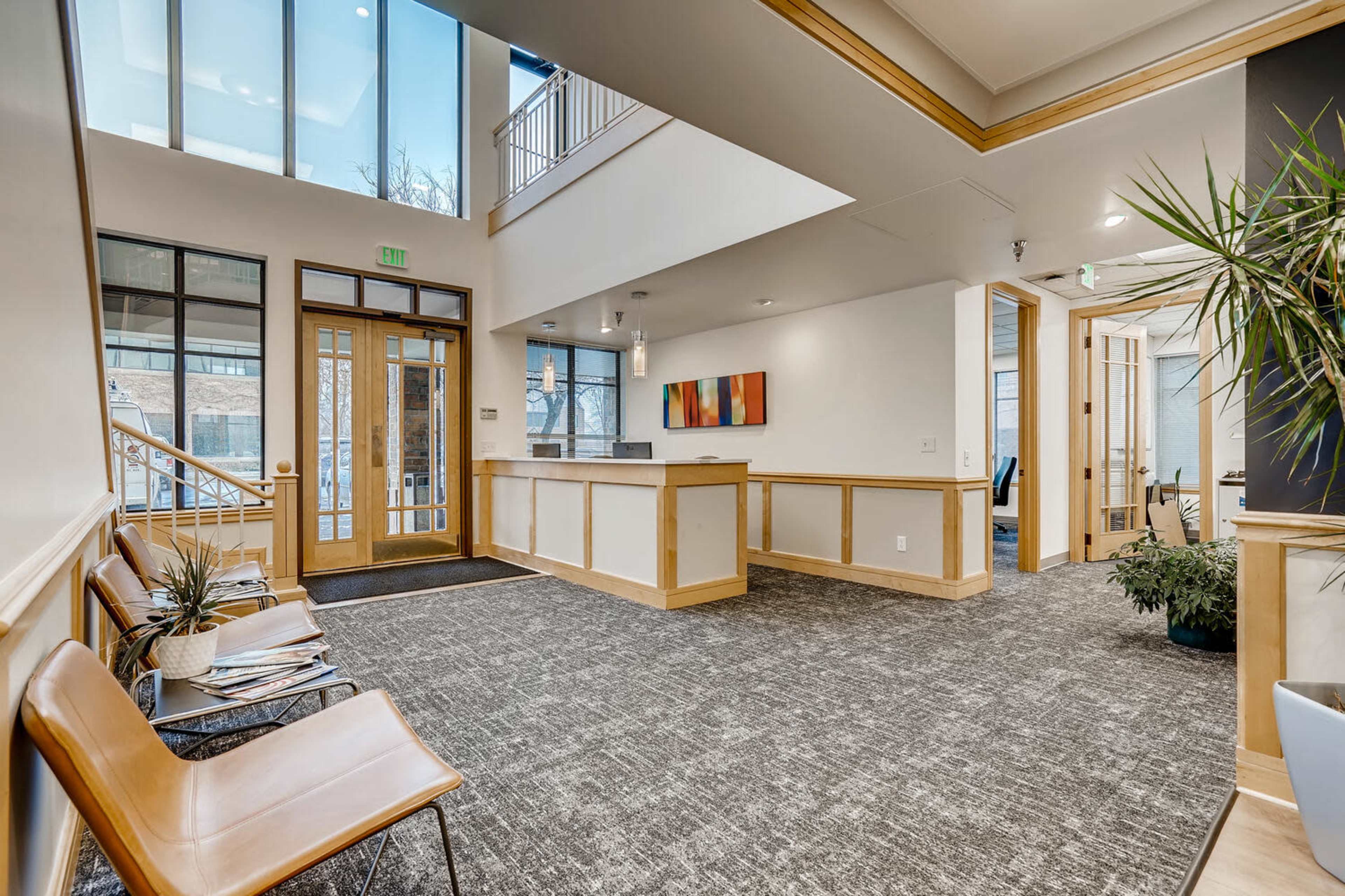 A modern reception area with seating, a service desk, and large windows allowing natural light to enter.