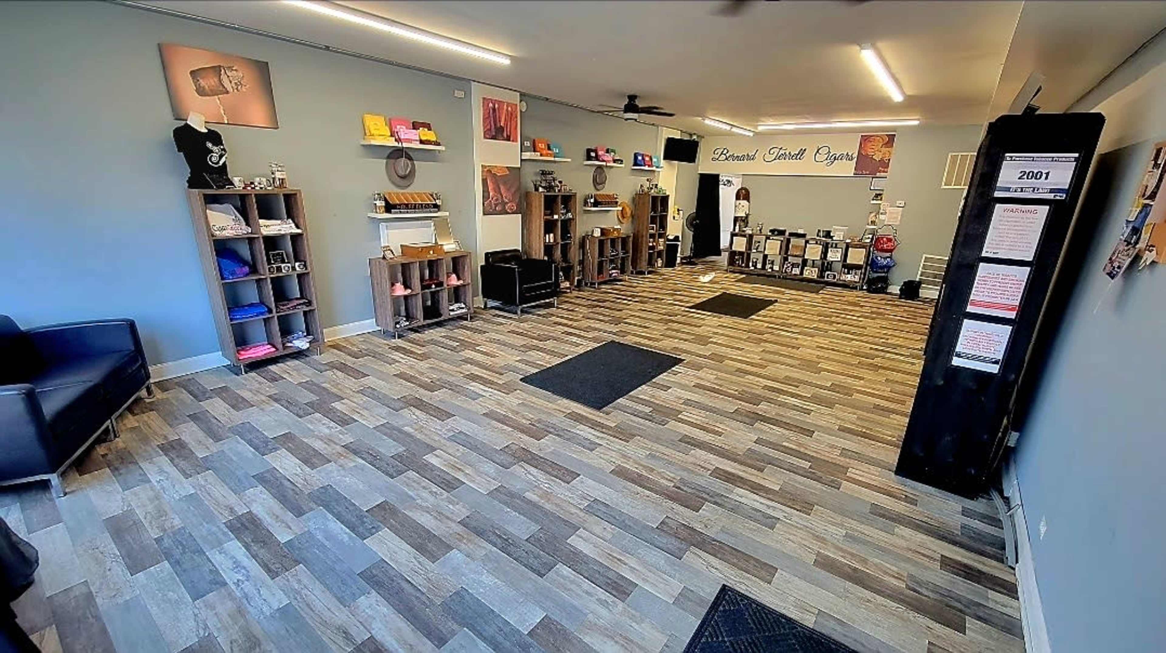 The image shows an interior of a spacious, organized studio with wooden flooring, shelves displaying various items, and a seating area.