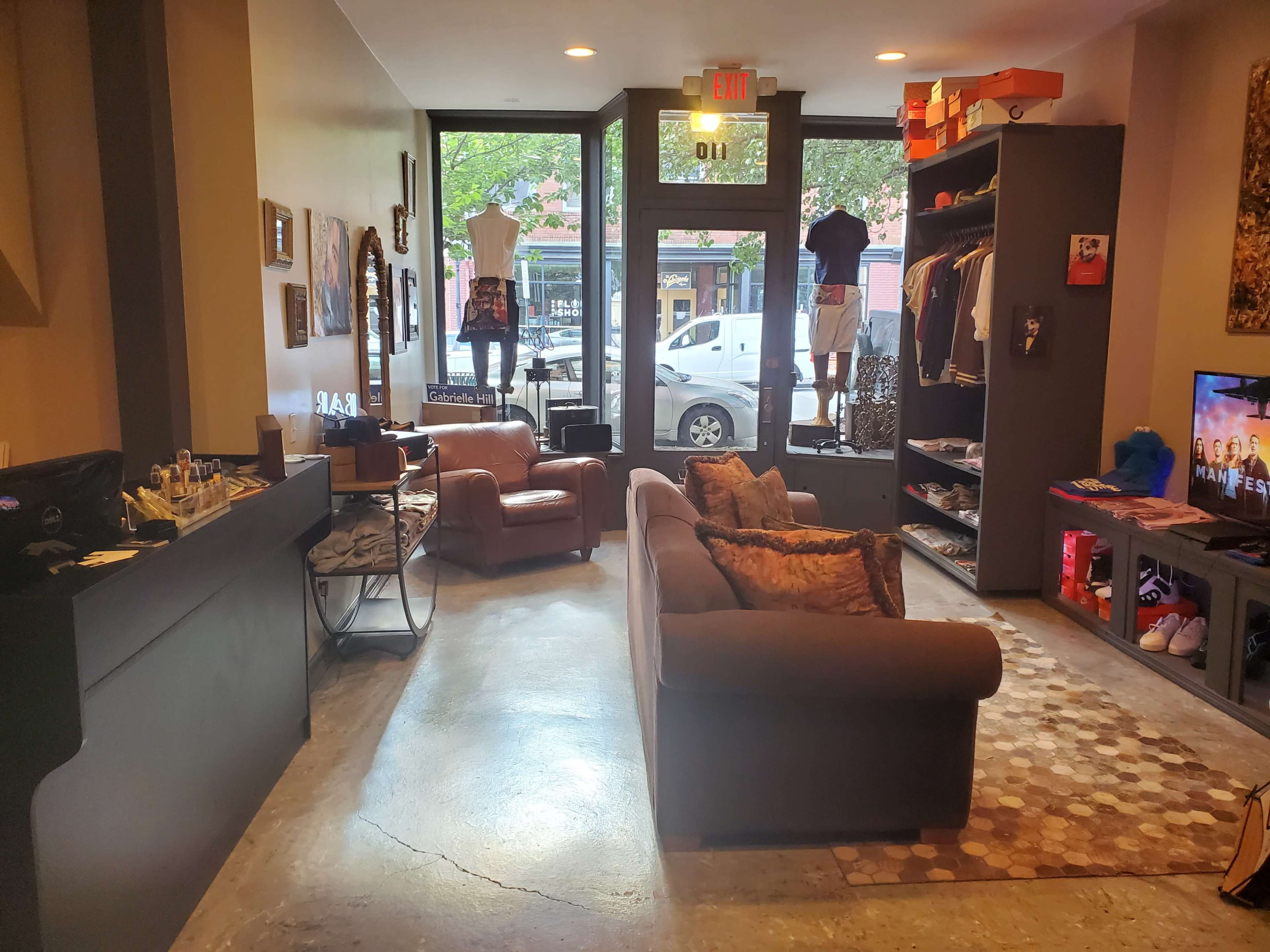 An interior of a retail store featuring a seating area, displays of clothing on mannequins, and a merchandise rack along the walls.