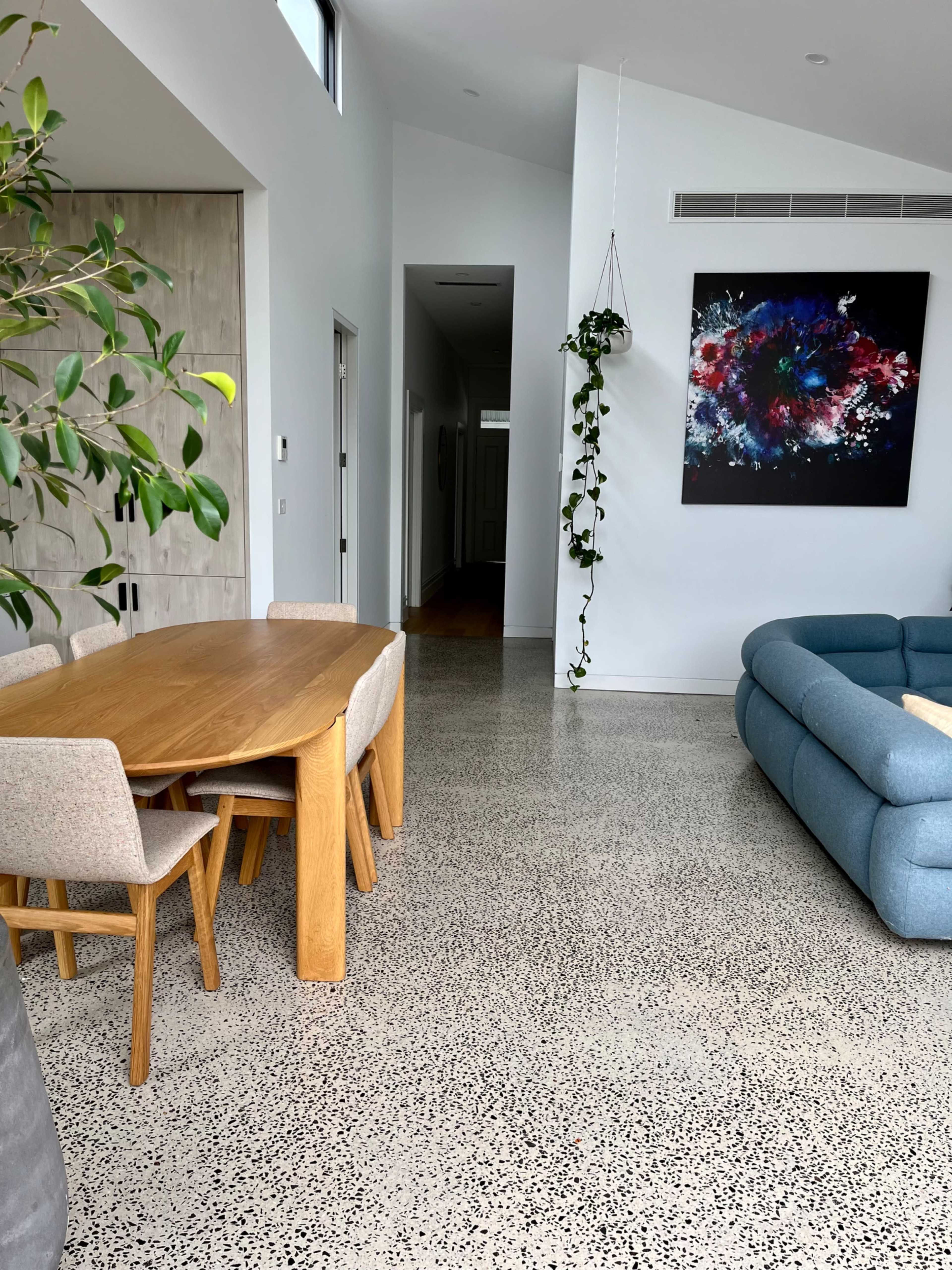 A modern living space with a dining area featuring a wooden table and four chairs, a blue sectional sofa, and a wall adorned with a colorful abstract painting.