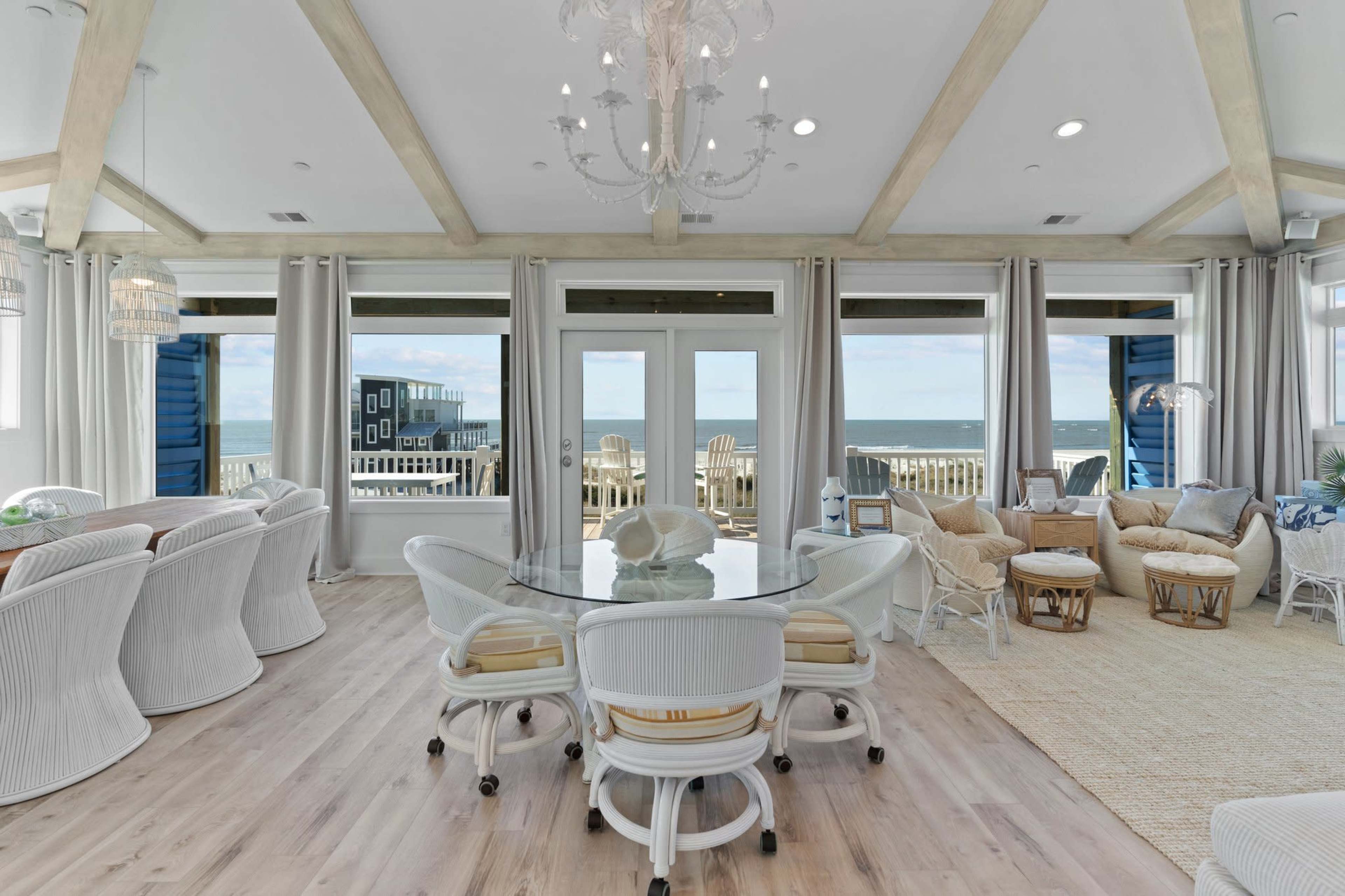A bright, airy living space with large windows overlooking the ocean, a round dining table surrounded by white chairs, and cozy seating areas.