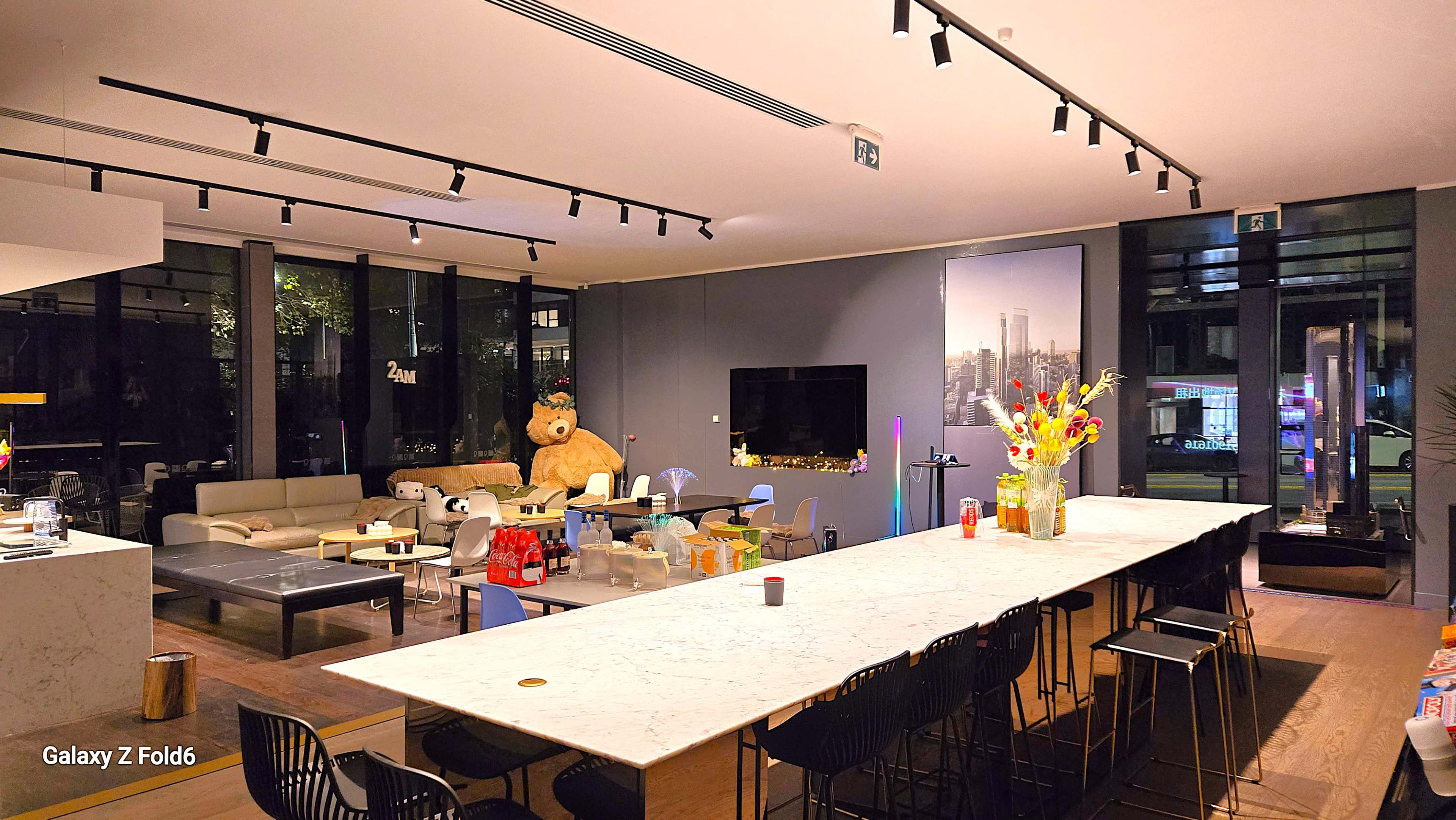 The image shows a modern living space with a long marble countertop, seating areas, a large television, and a decorative bear in the background.