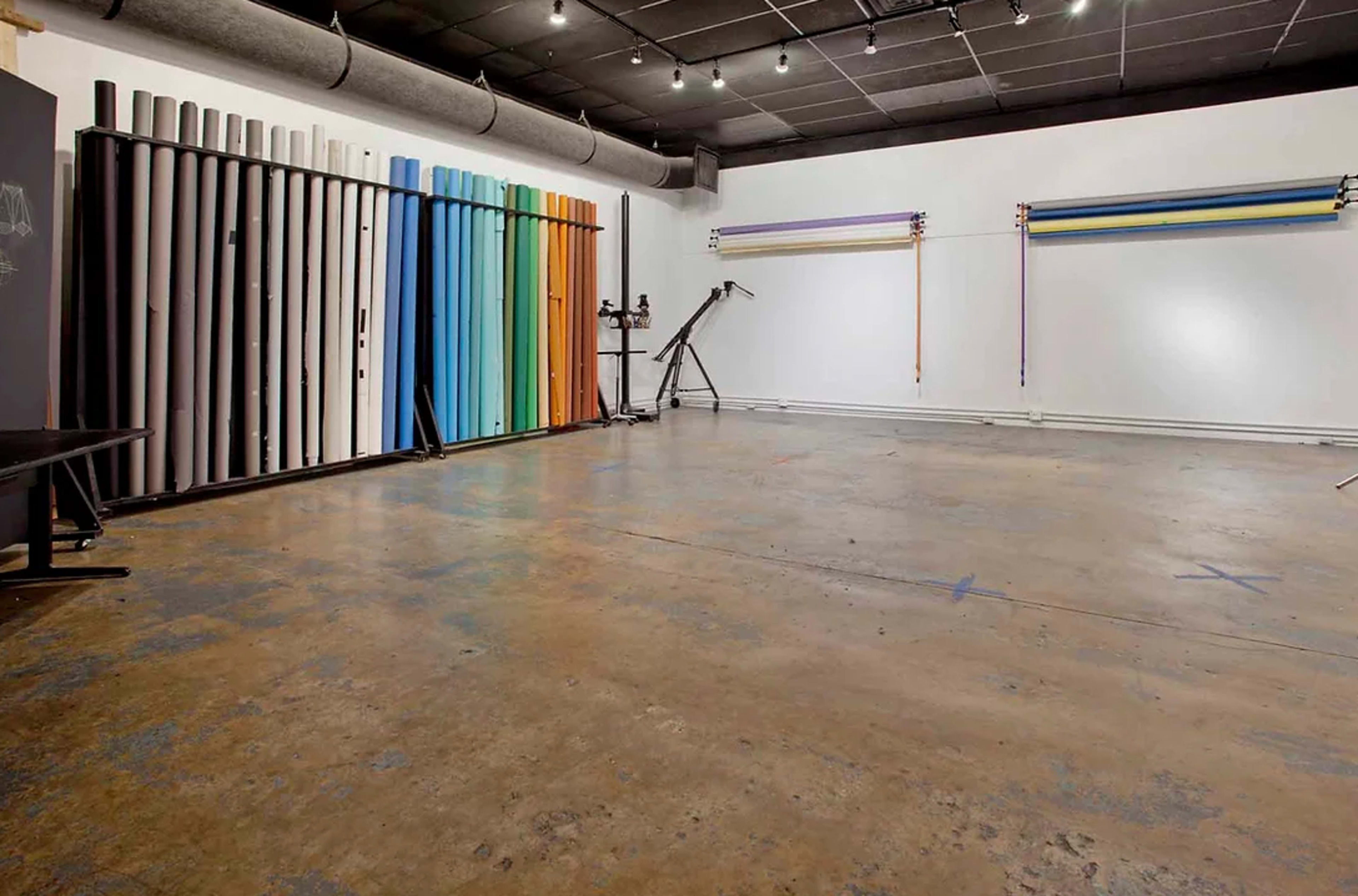 A spacious, empty studio with various colored backdrops hung on the walls and a polished concrete floor.