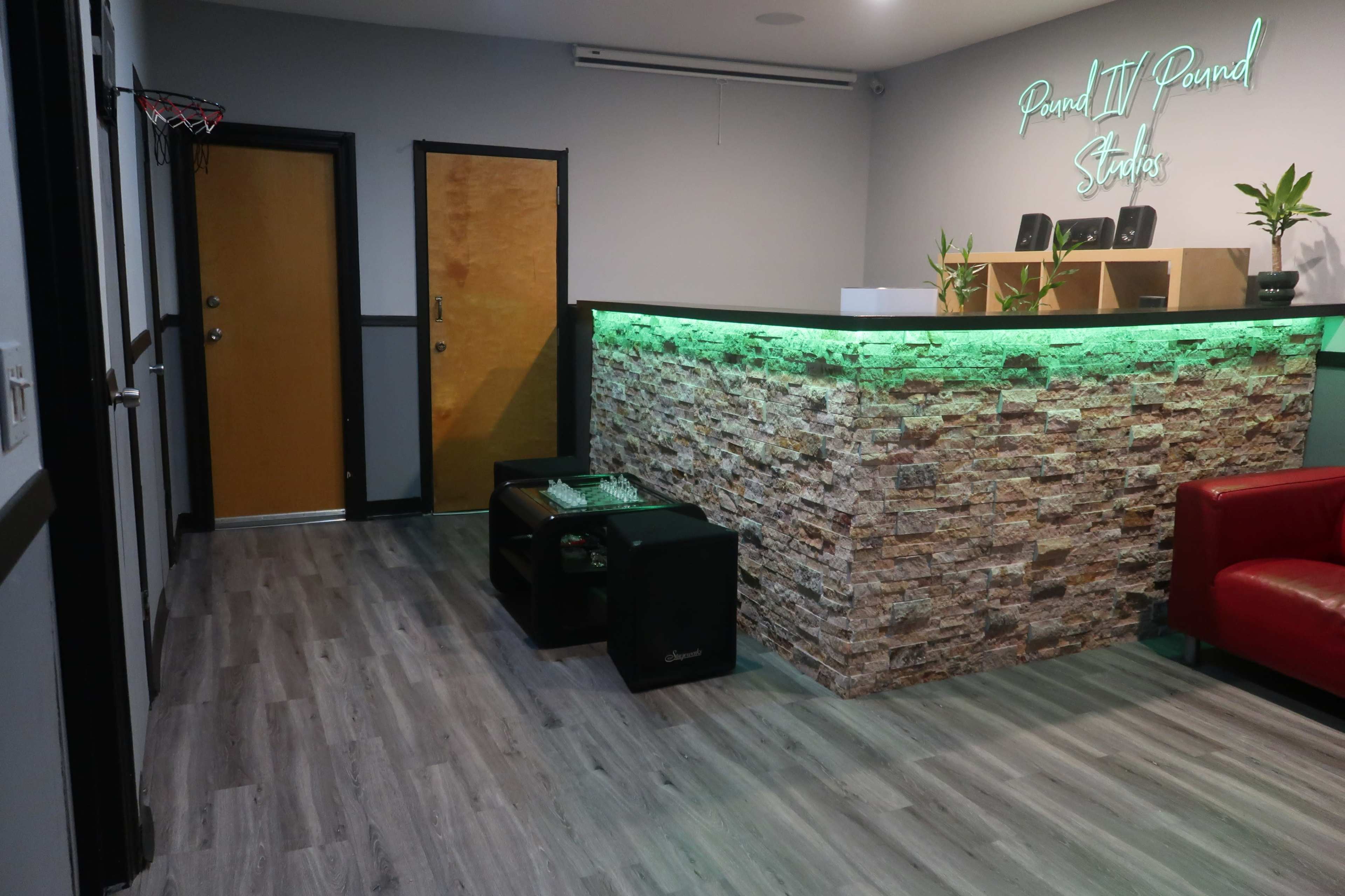 The image shows a modern reception area with a stone accent wall, green lighting, and a red couch, featuring a basketball hoop in the corner.