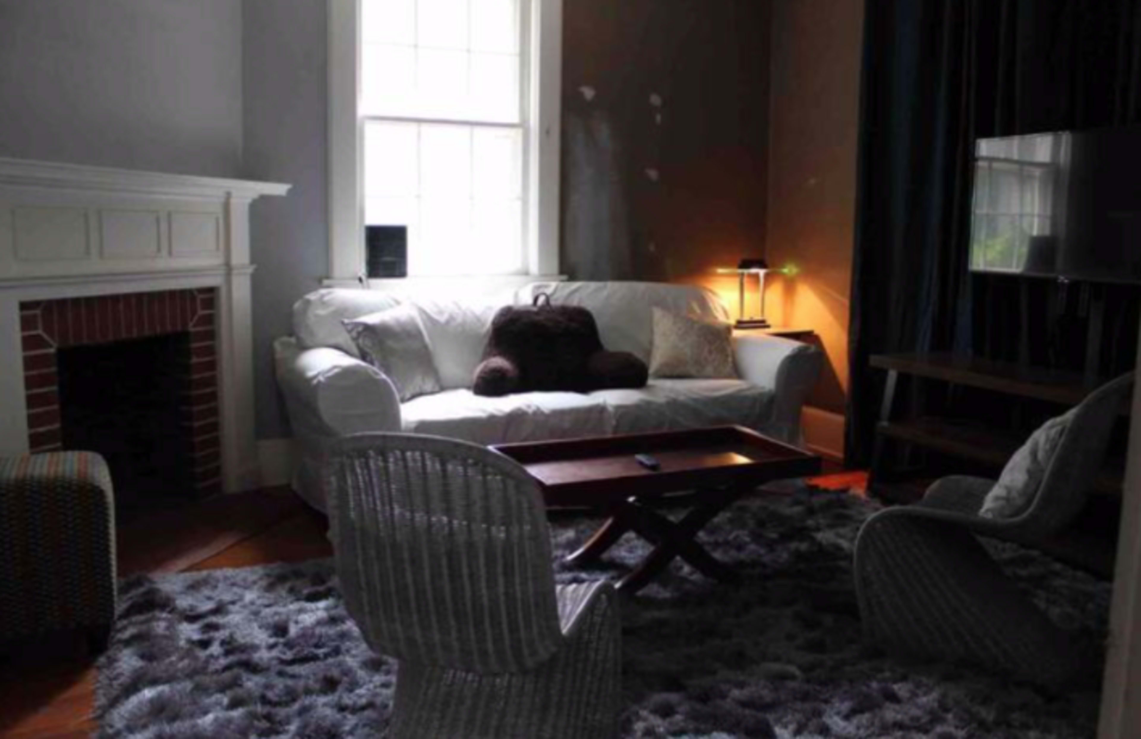 A living room with a white sofa, a wooden coffee table, and two woven chairs, all arranged on a plush rug beside a fireplace and a wall-mounted television.